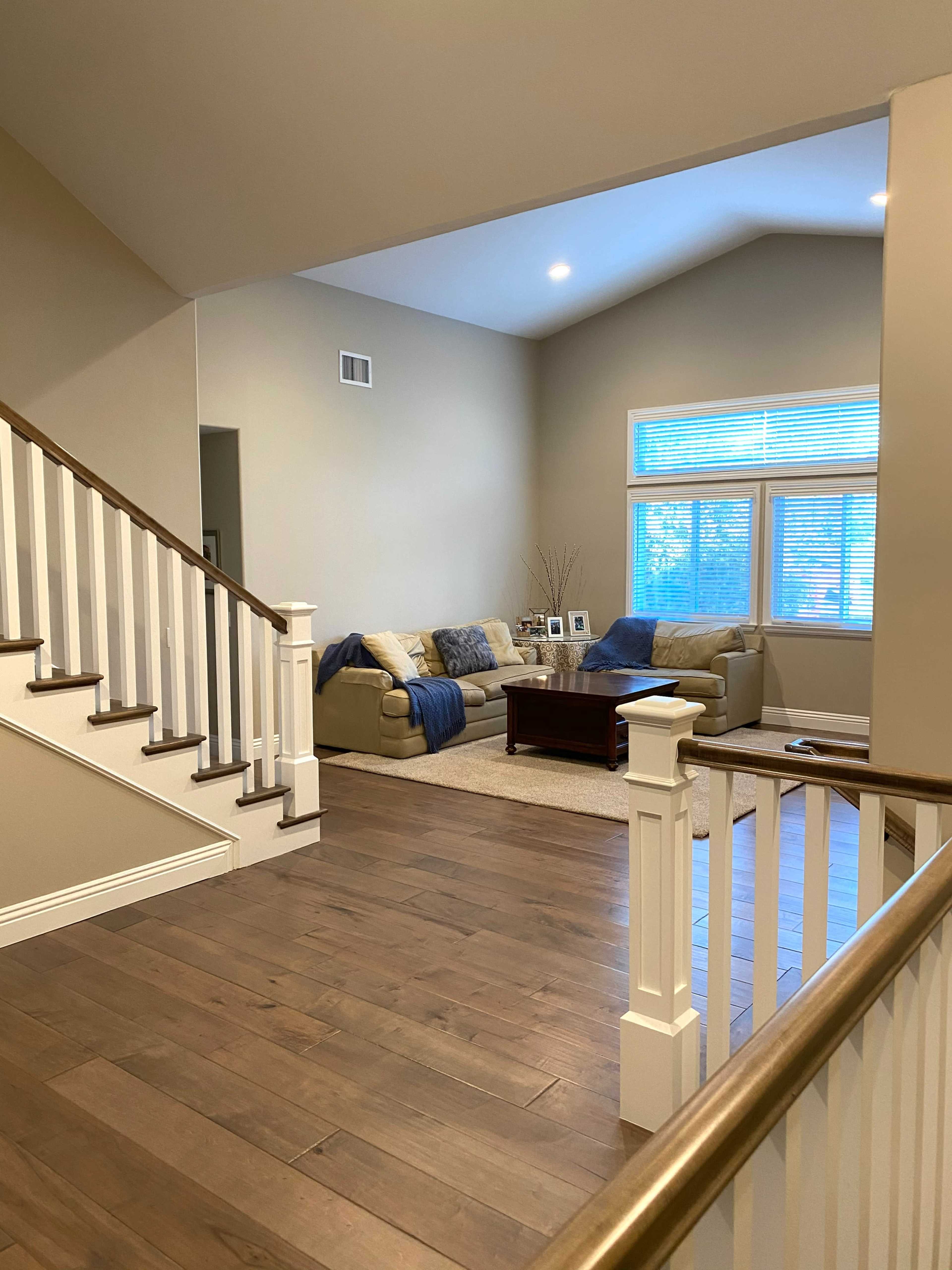 A staircase leads to a living room with a cozy seating area, large windows, and a coffee table.