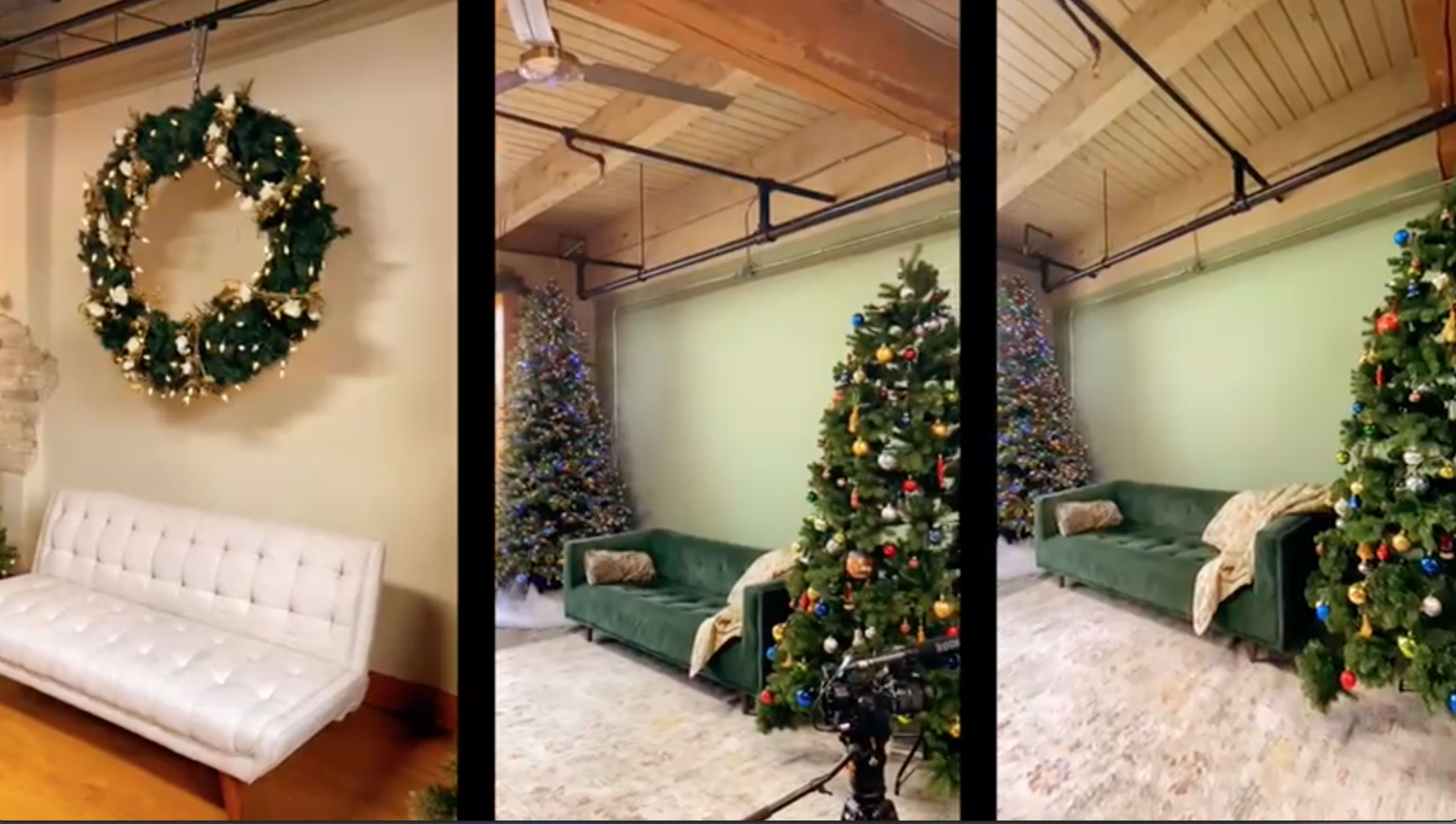A decorated living space with a large wreath on the wall and two Christmas trees, one on each side, beside a white couch.