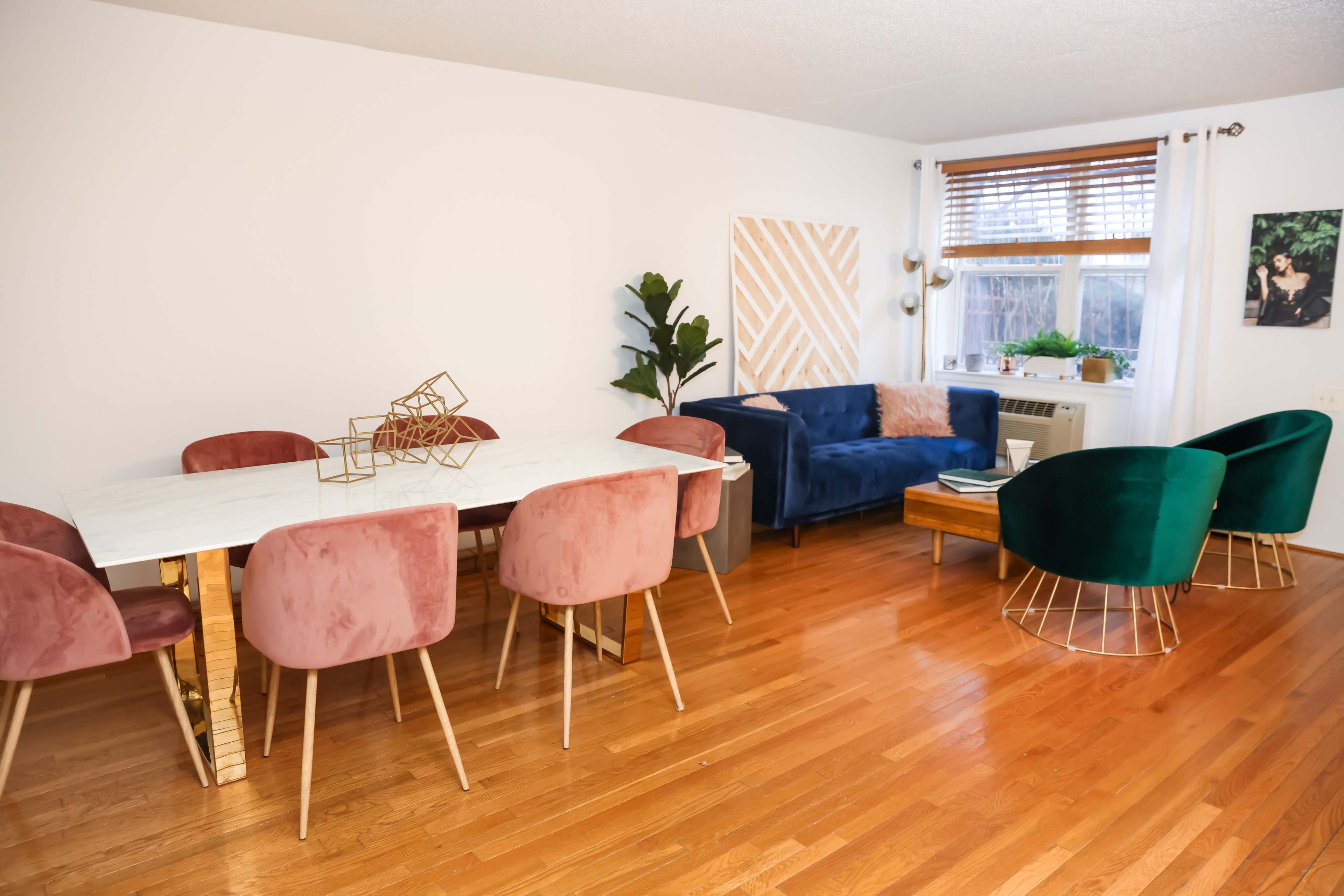 A modern living space features a marble dining table surrounded by pink chairs, with a blue couch and green accent chairs positioned nearby.