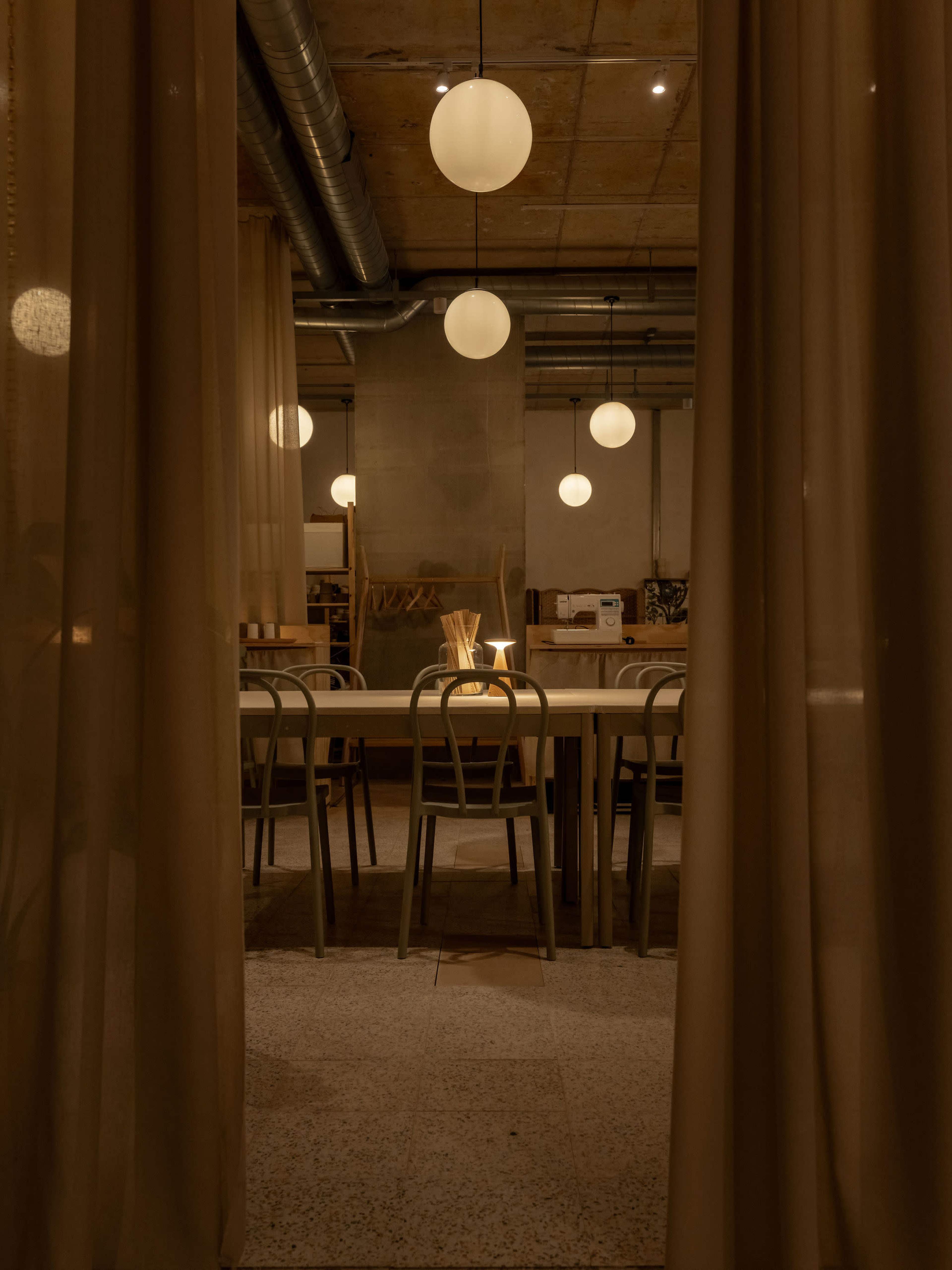 A dimly lit dining area features a long table surrounded by chairs, illuminated by round pendant lights hanging from the ceiling.