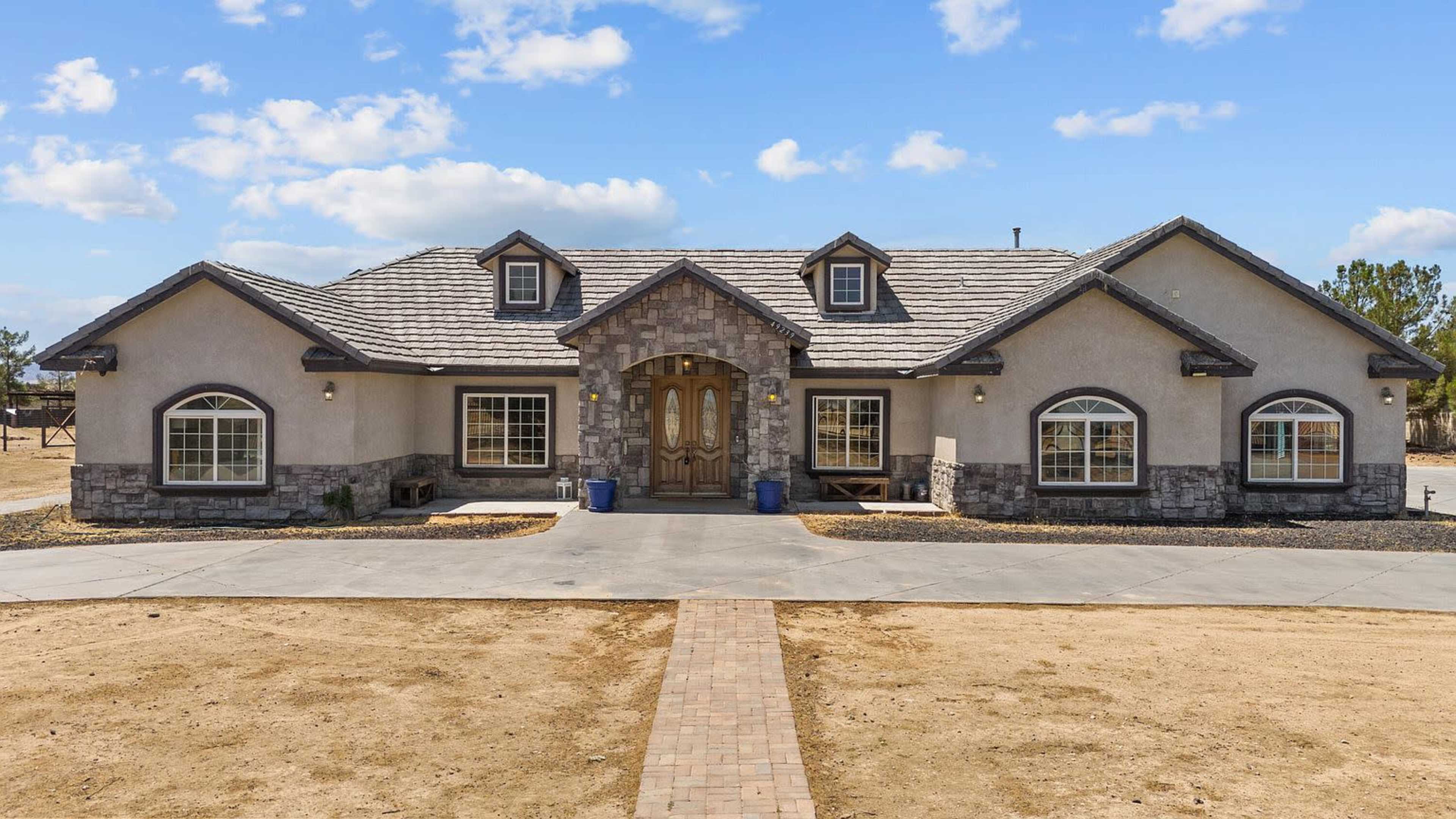 A single-story house with a stone facade features a central entrance and arched windows on each side, set against a clear blue sky.