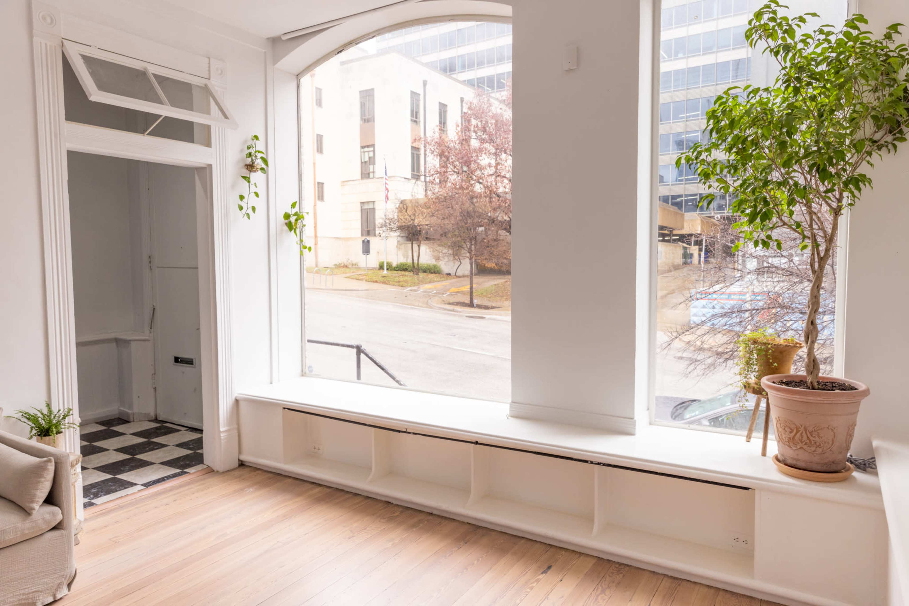 A bright, spacious interior with a large arched window, a potted plant, and a checkered black-and-white floor near the entrance.
