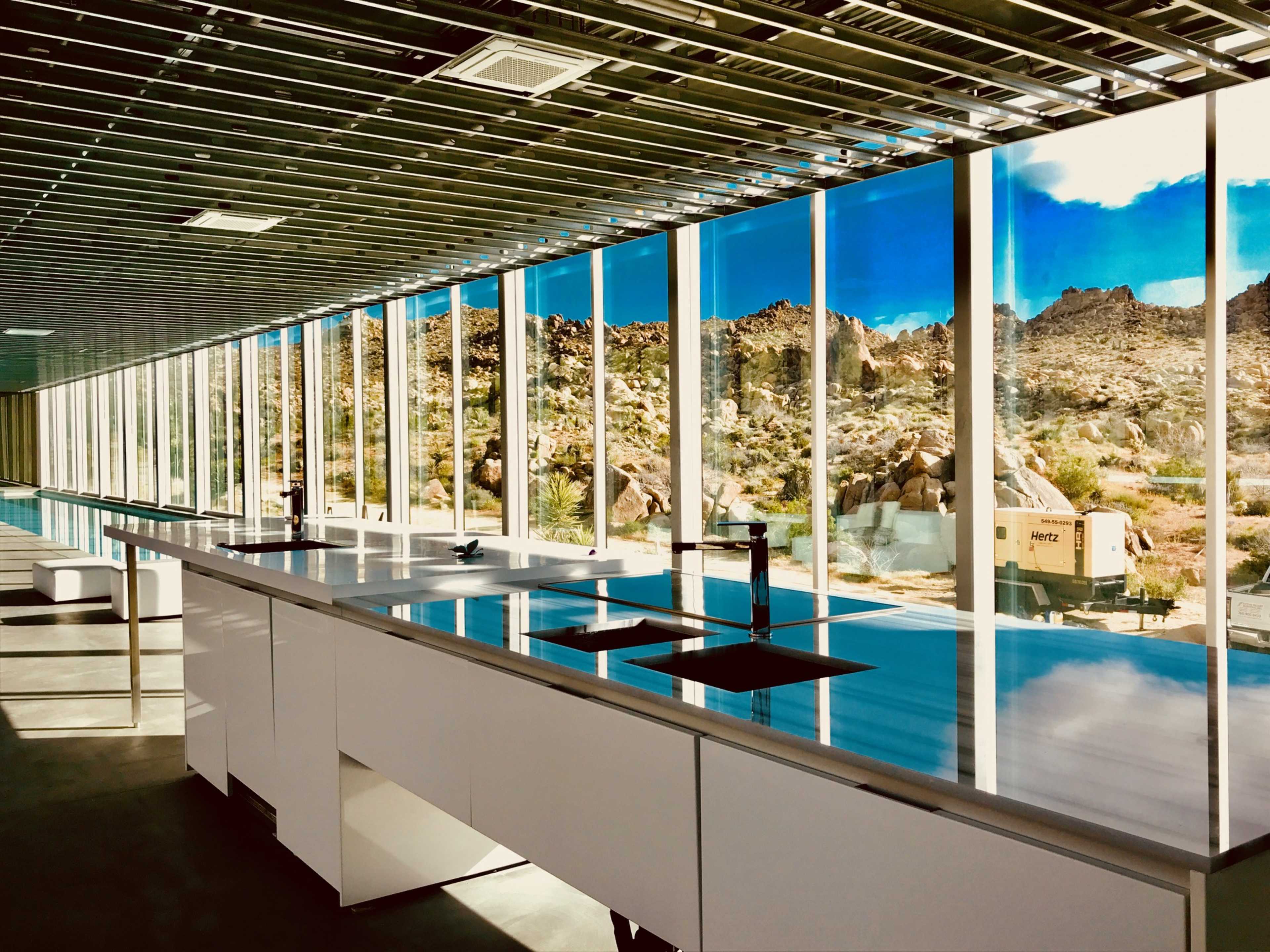A modern kitchen with sleek white cabinets and large windows overlooking a desert landscape with rocky terrain.