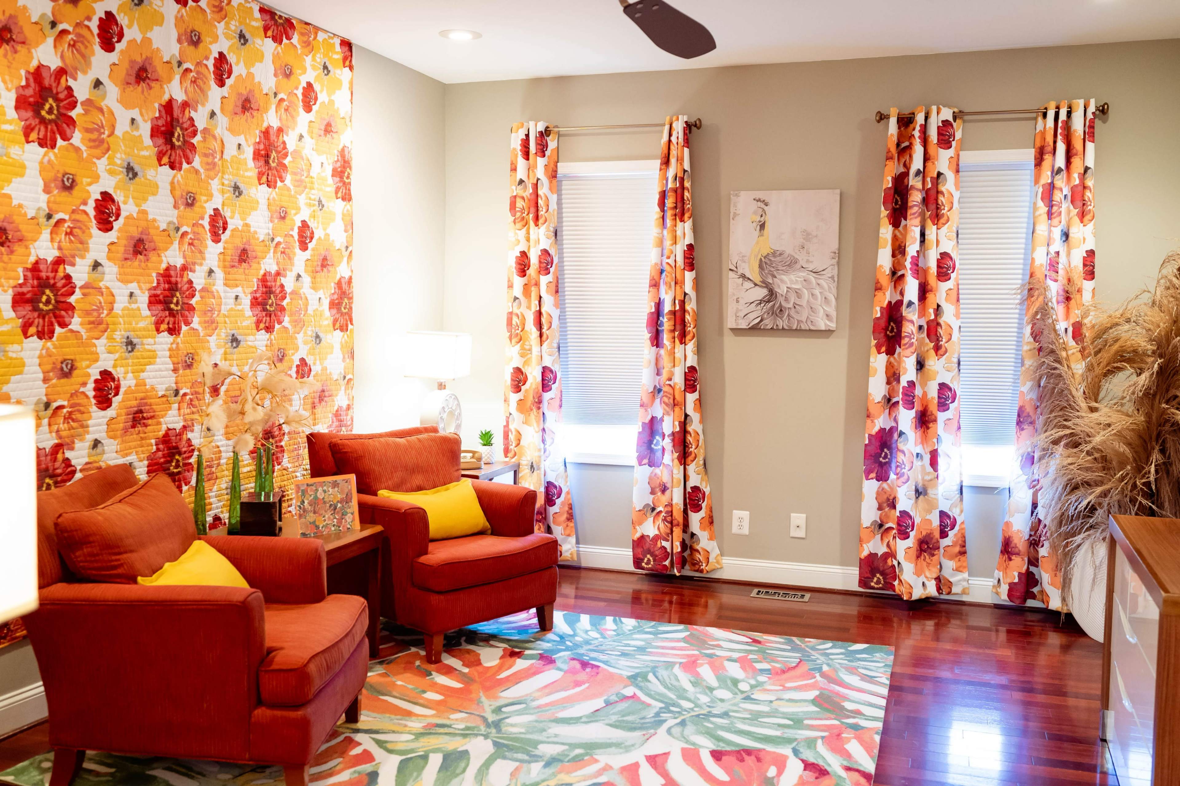 The room features two red armchairs and colorful floral curtains, with a wall covered in a similar floral pattern and a painting on one wall.