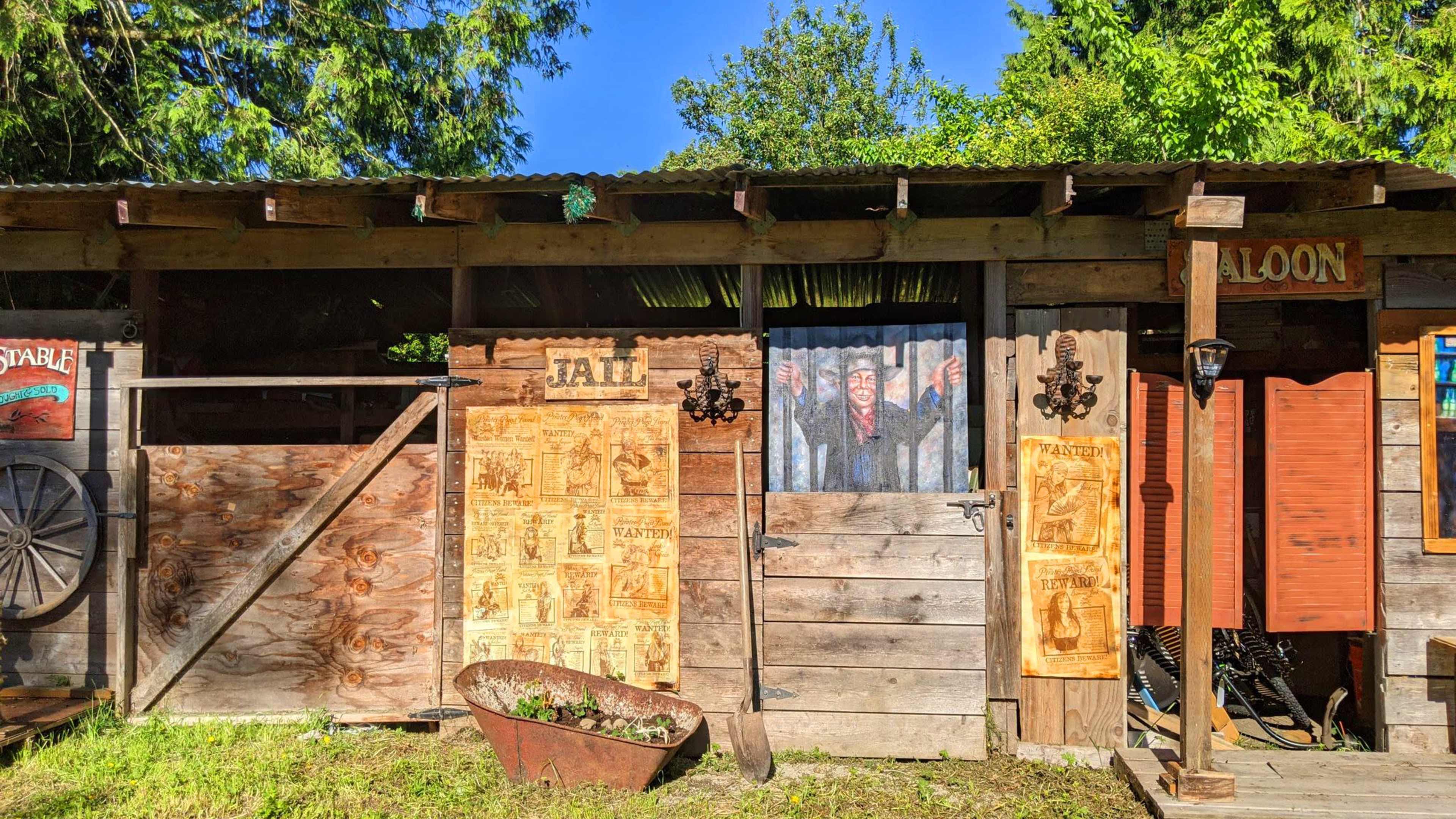 The scene features a rustic wooden structure with a barred jail door and detailed old posters on the walls, set against a backdrop of greenery.
