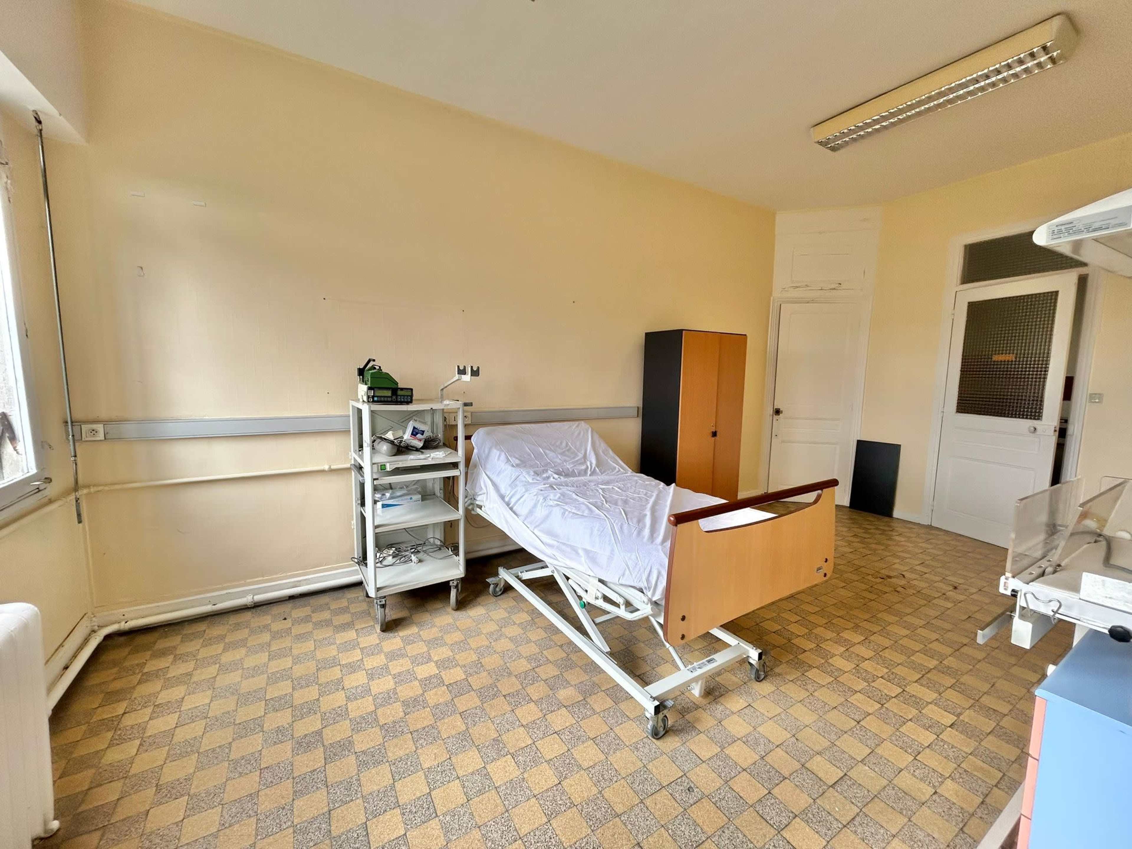 A hospital room with a bed, a medical cart, and a cabinet against the wall.