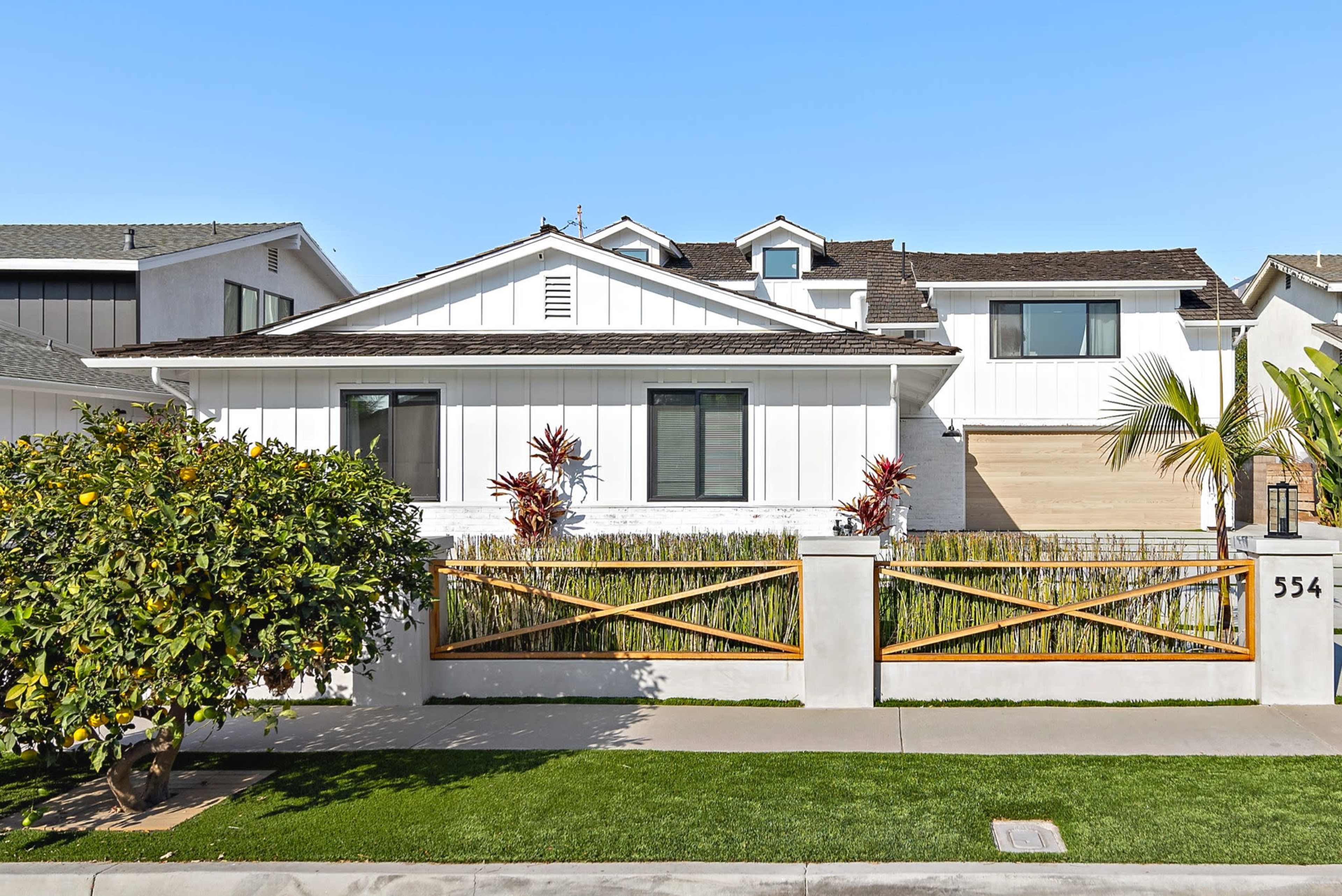 A white, modern-style house with a garden is visible behind a wooden fence and a pathway lined with grass.