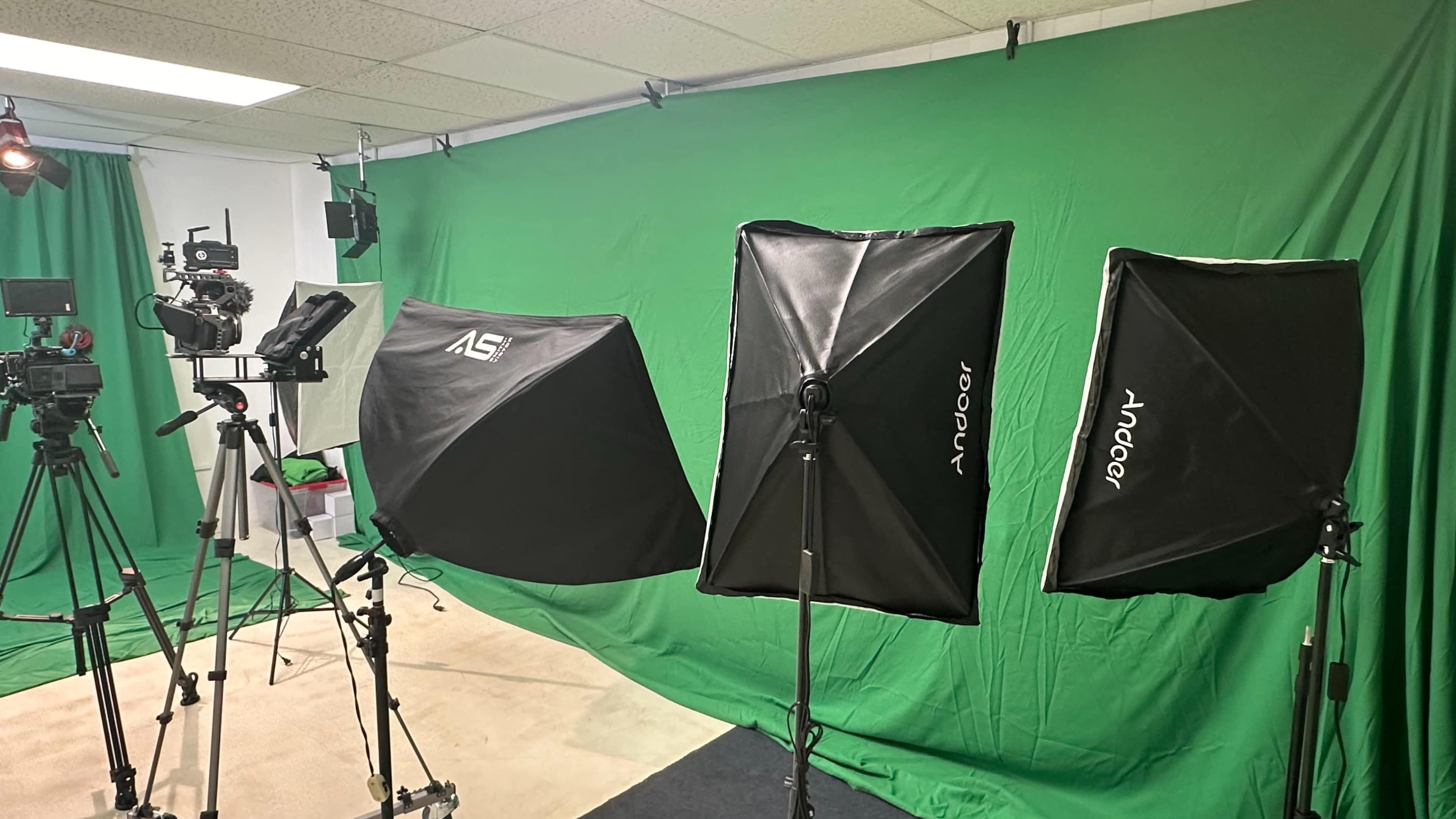 A green screen studio setup with three softbox lights and various camera equipment.