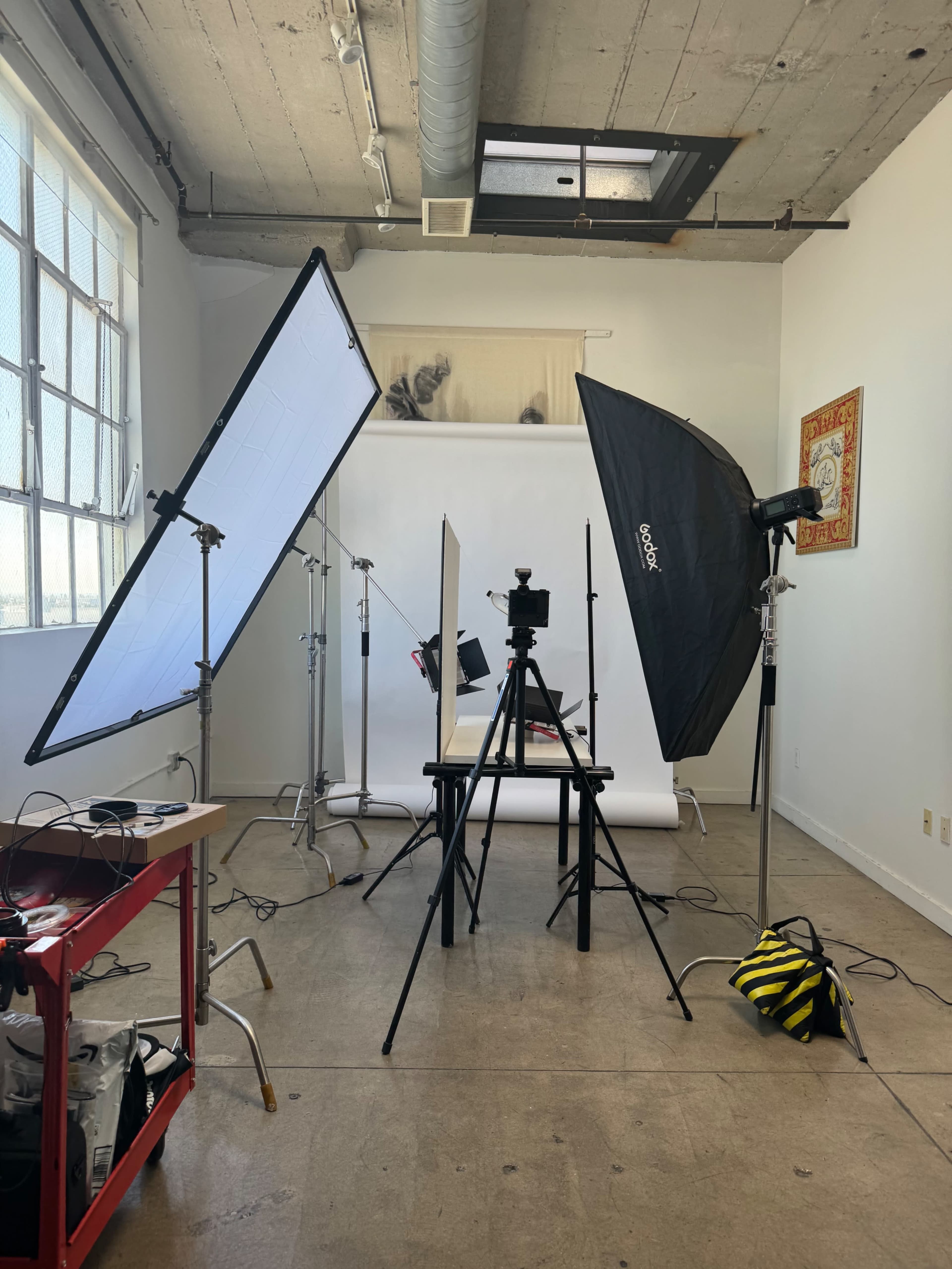 A photography studio setup with three light sources, a camera on a tripod, and a table surrounded by backdrops.