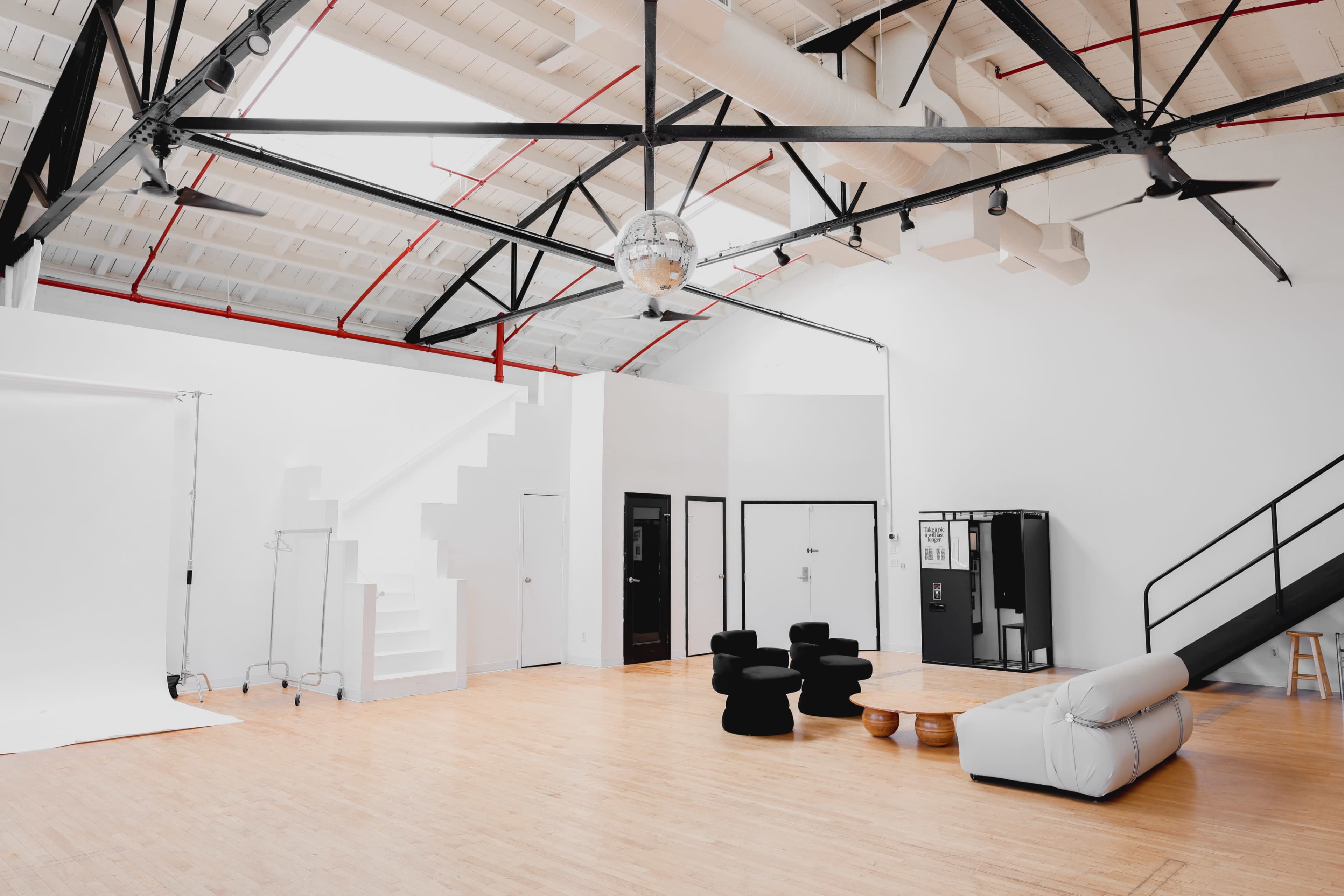 A spacious, modern interior with high ceilings, featuring a staircase, black furniture, a white sofa, and a large disco ball hanging from the ceiling.