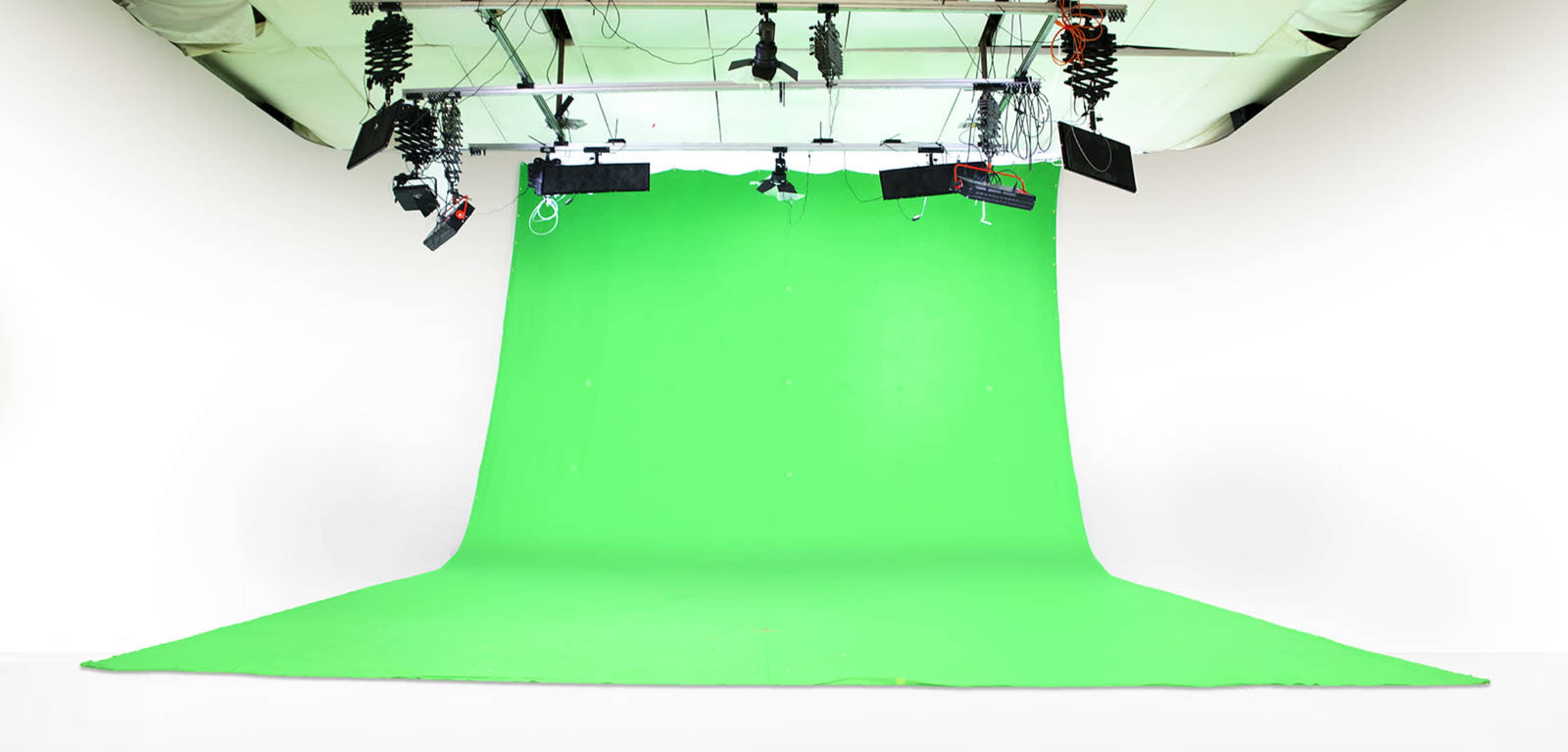 A spacious studio with a large green backdrop and various lighting equipment hanging from the ceiling.