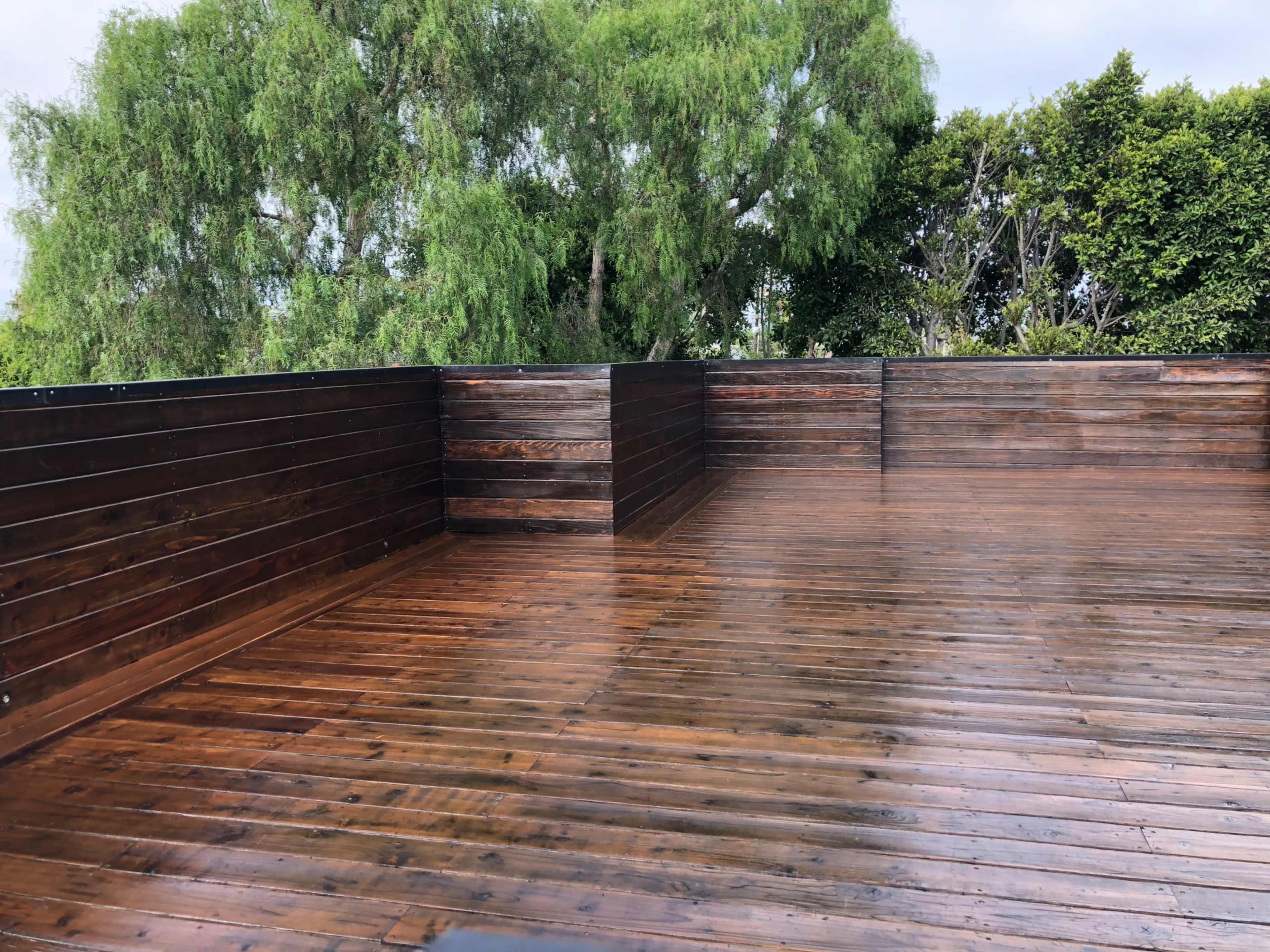 The image shows a wooden deck with a polished surface surrounded by greenery.
