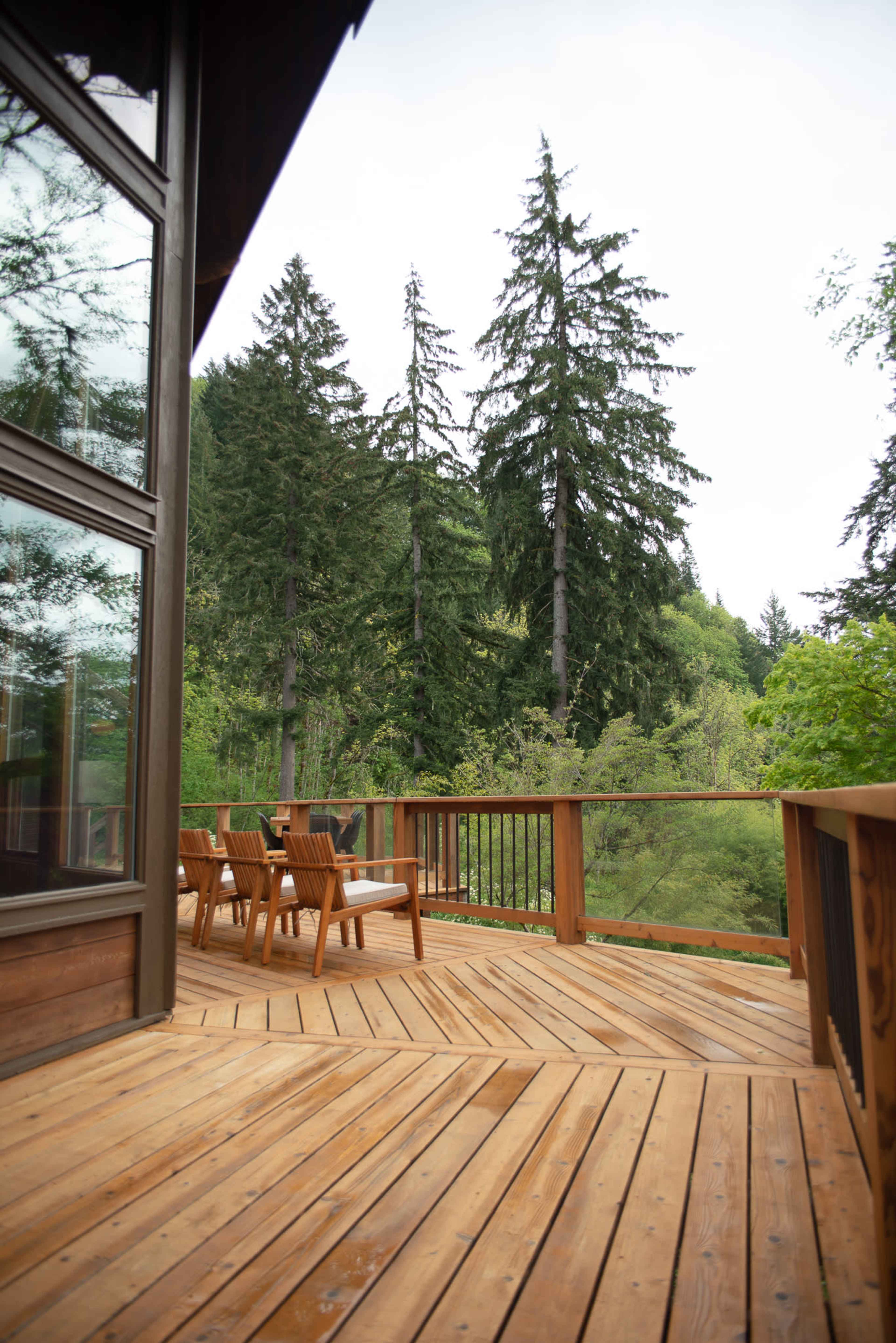 A wooden deck with outdoor seating overlooks a forested area with tall trees.
