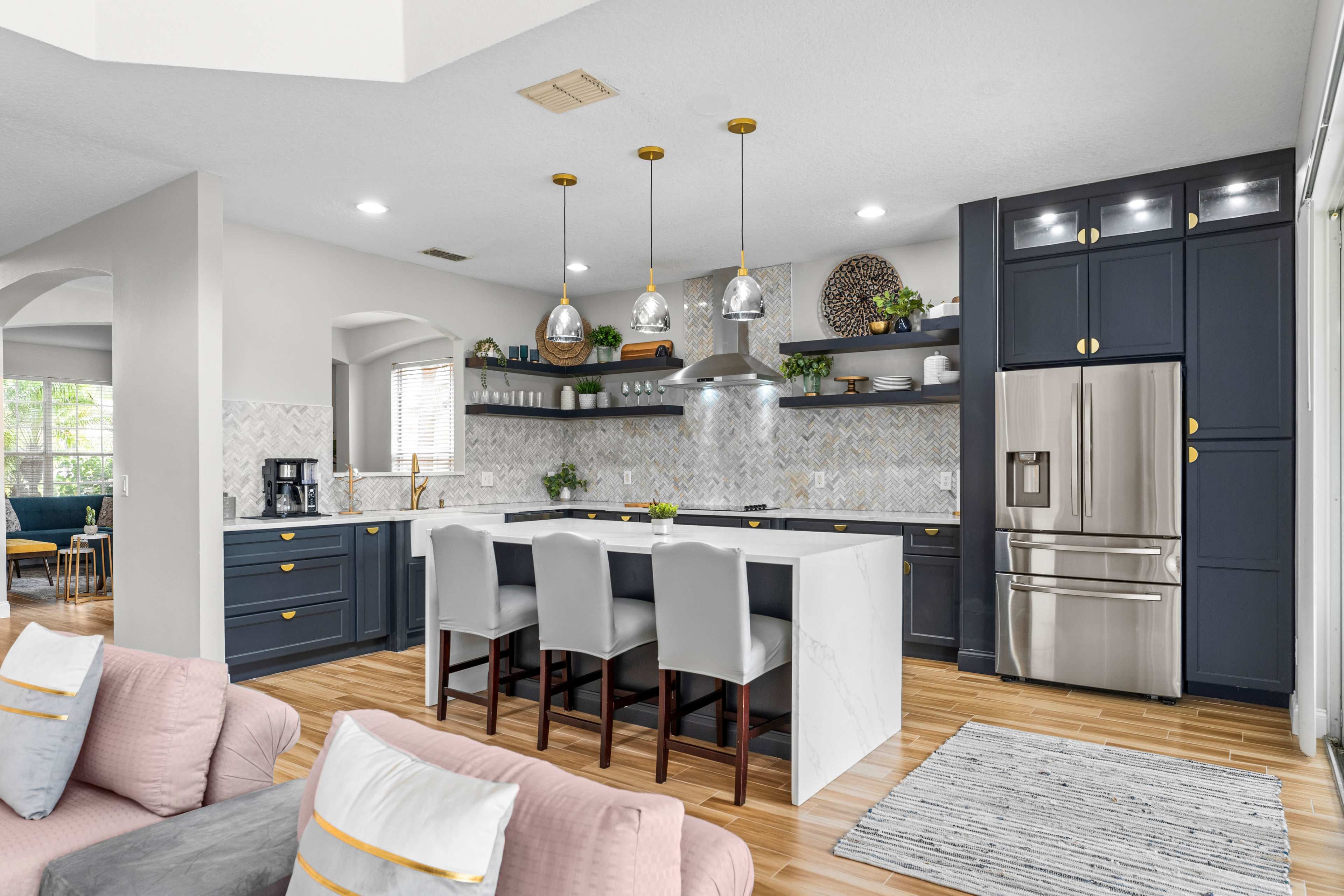 A modern kitchen features dark blue cabinets, a central island with white marble, pendant lights, and stainless steel appliances.