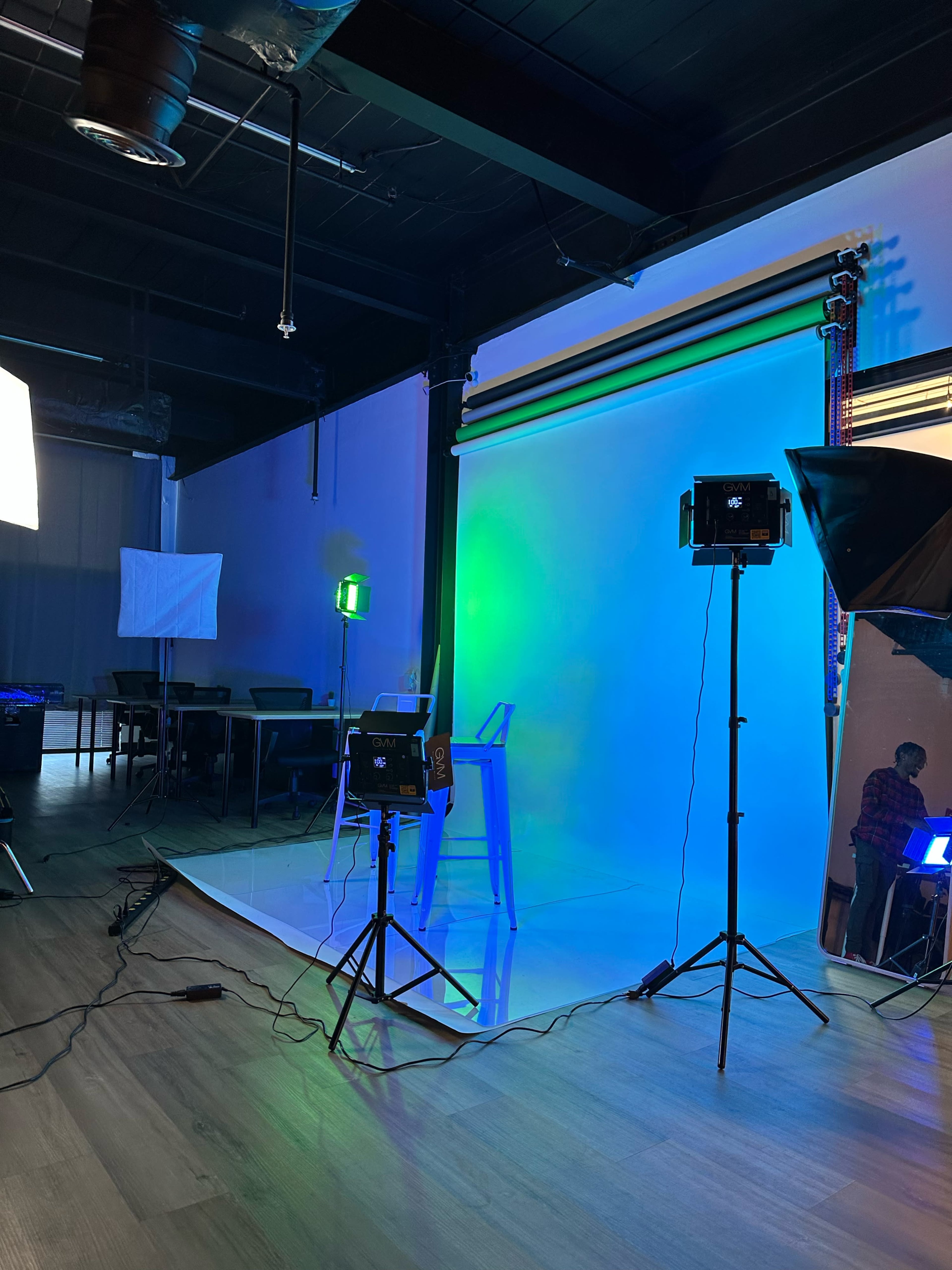 A studio setup with various lighting equipment and a blue-green backdrop, accompanied by a bar stool on a white platform.