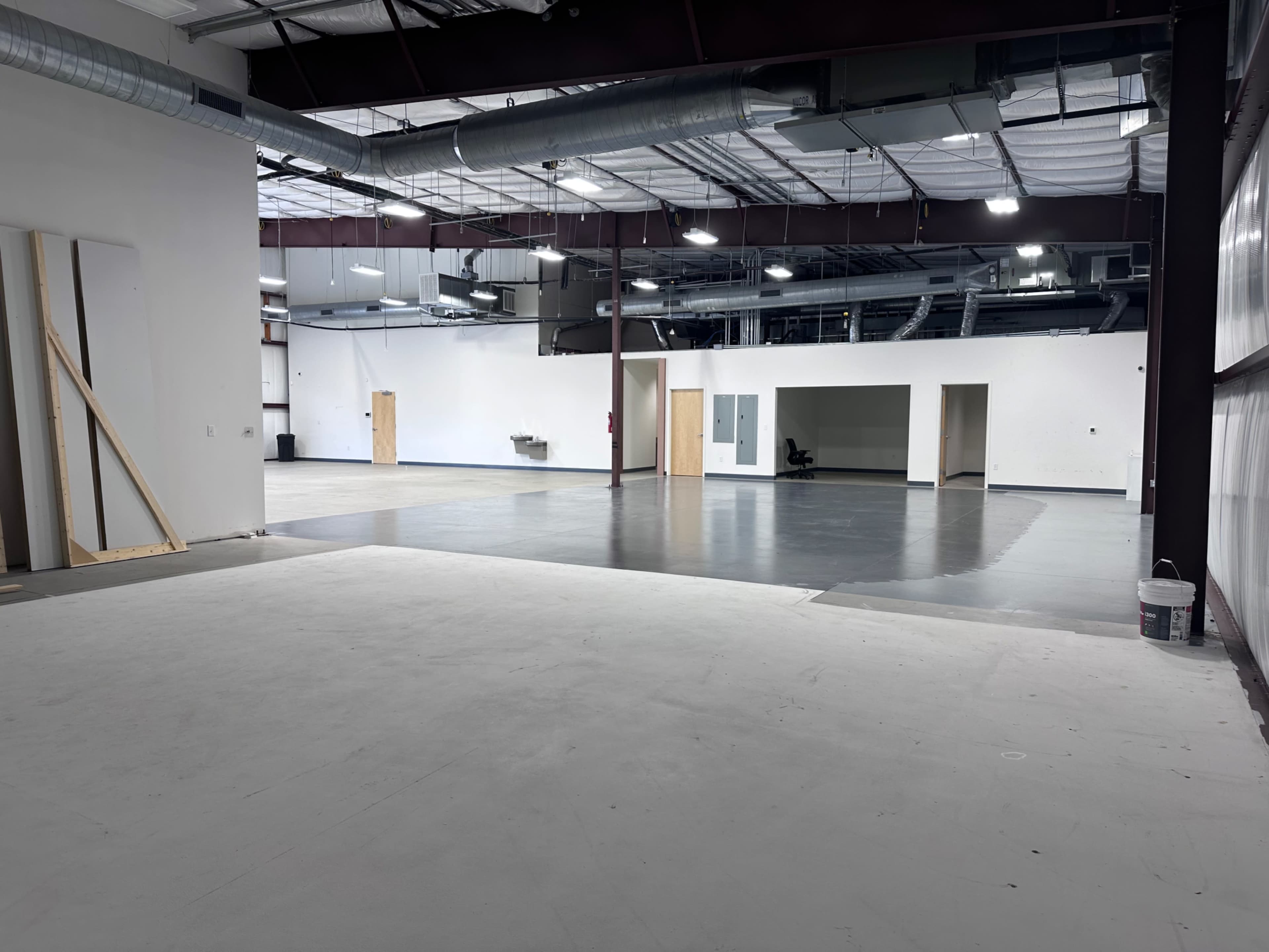 The image shows a spacious, unfinished commercial interior with concrete flooring, exposed ceilings, and multiple entry points.
