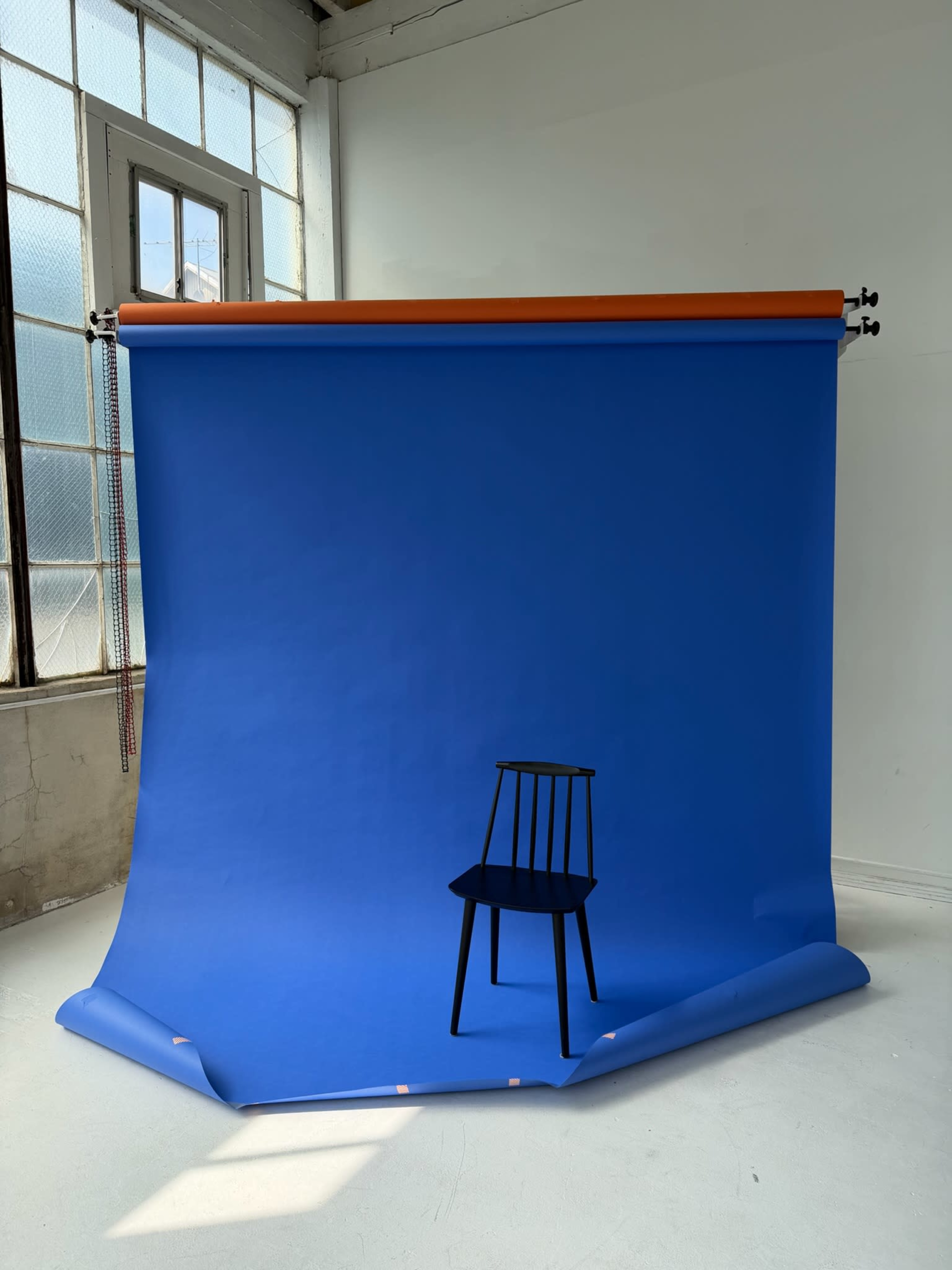 A black chair is placed in front of a bright blue backdrop in a well-lit room.