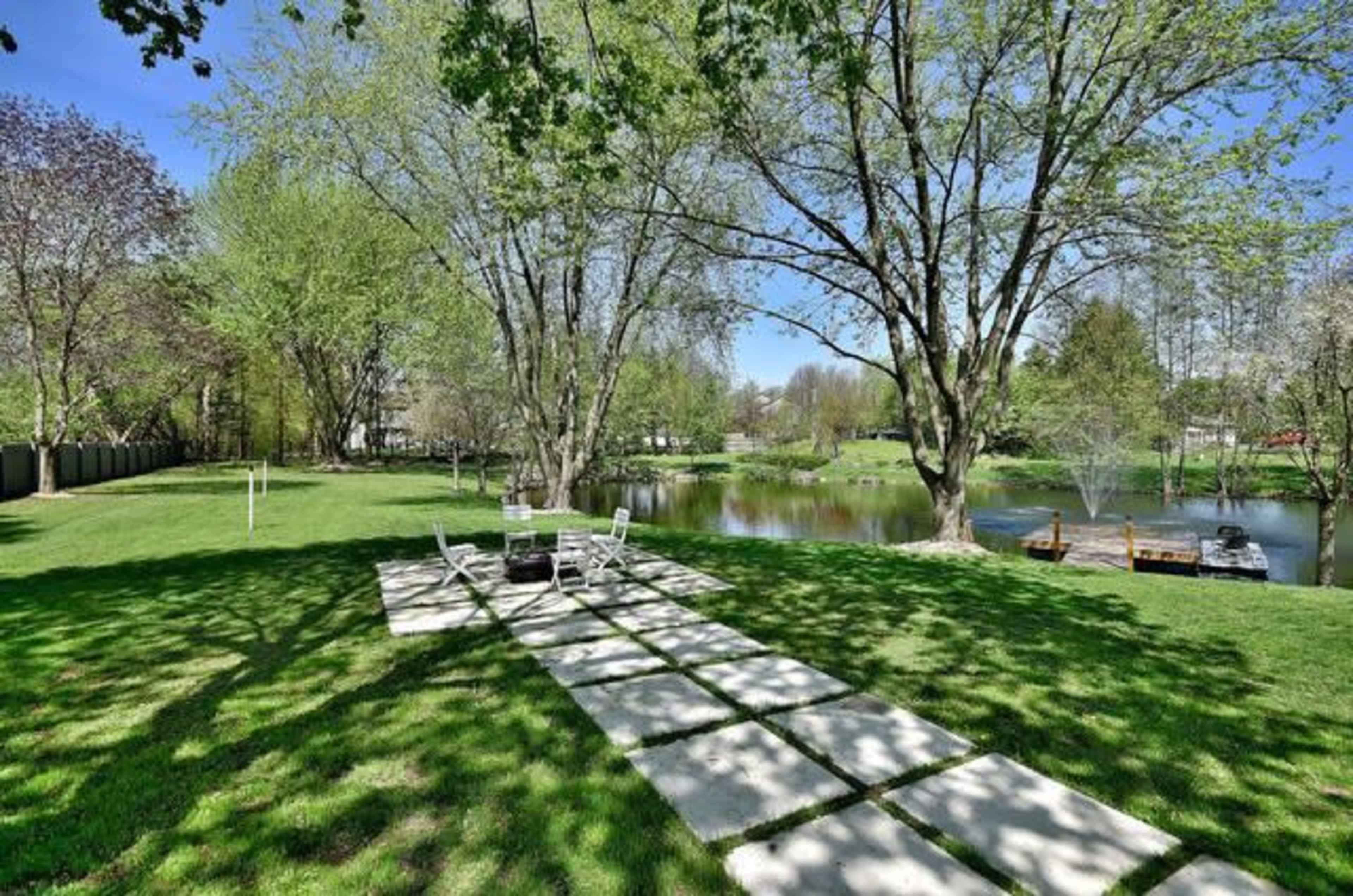 A grassy area with a stone pathway leading to a pond surrounded by trees.