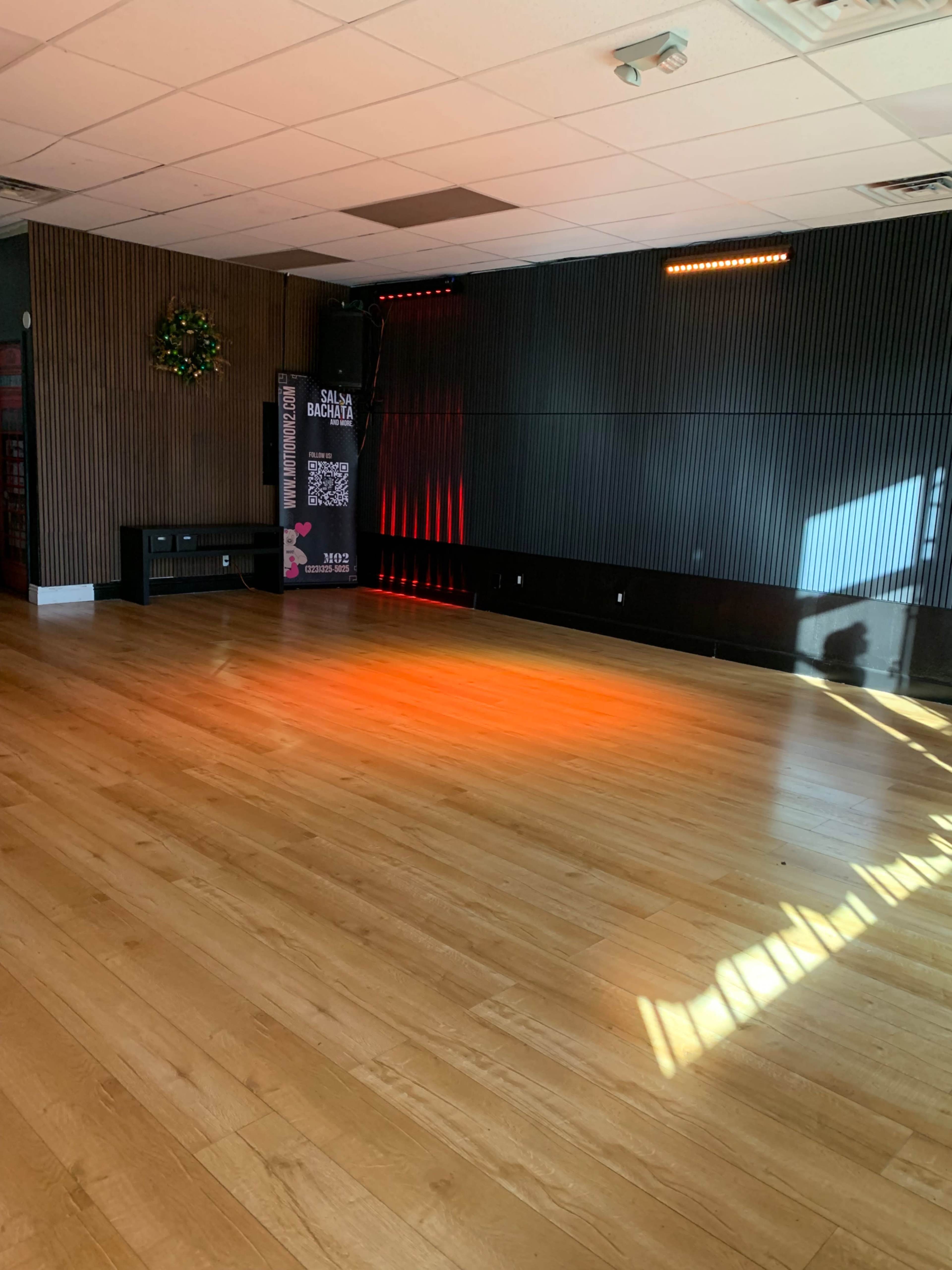 The image shows an empty dance studio with wooden flooring, a mirrored wall, and a spotlight casting light on one side of the room.