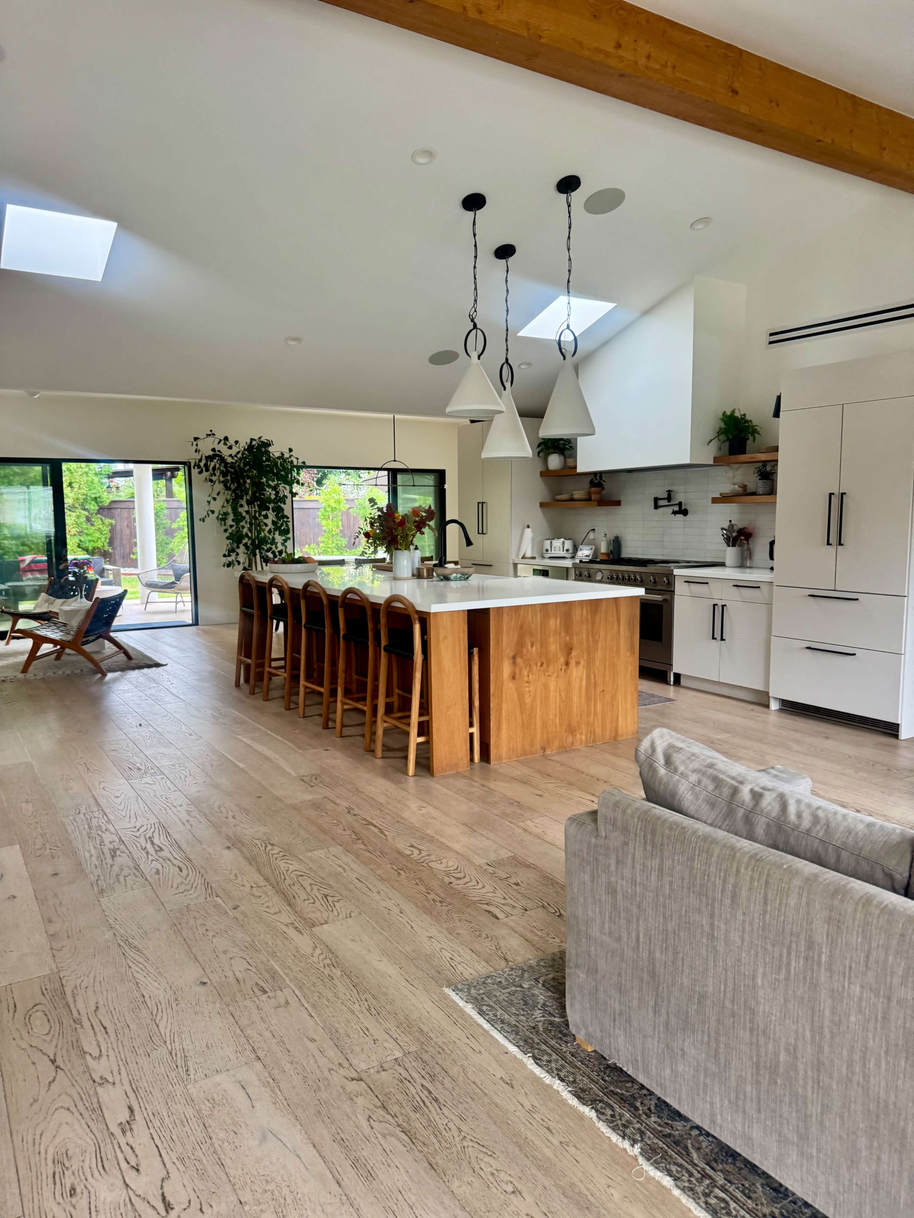 The image shows an open-concept modern kitchen with a large wooden island, bar stools, and a living area featuring a sofa and decorative rug.