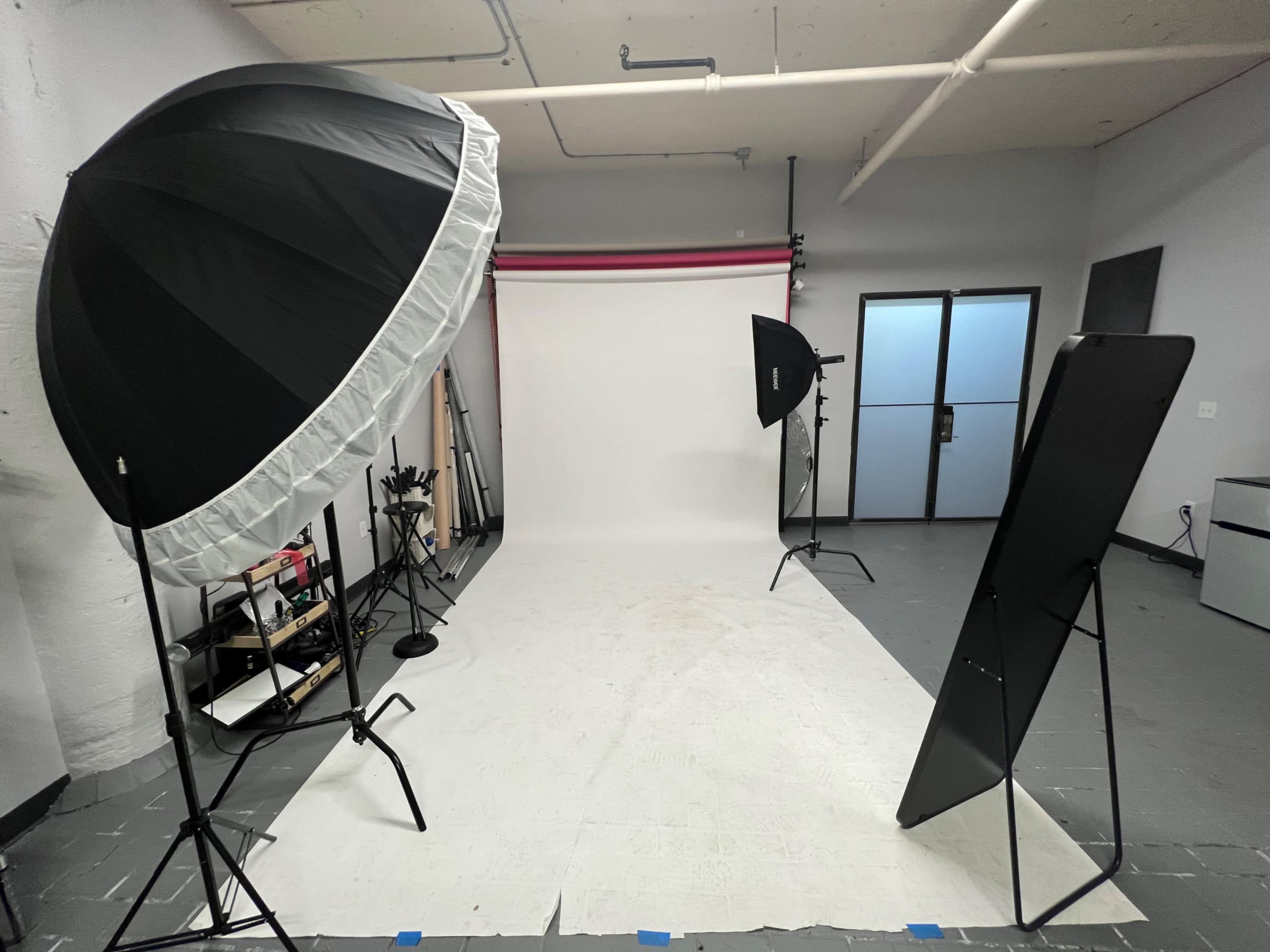 A photography studio with two light umbrellas, a large mirror, and a blank backdrop.
