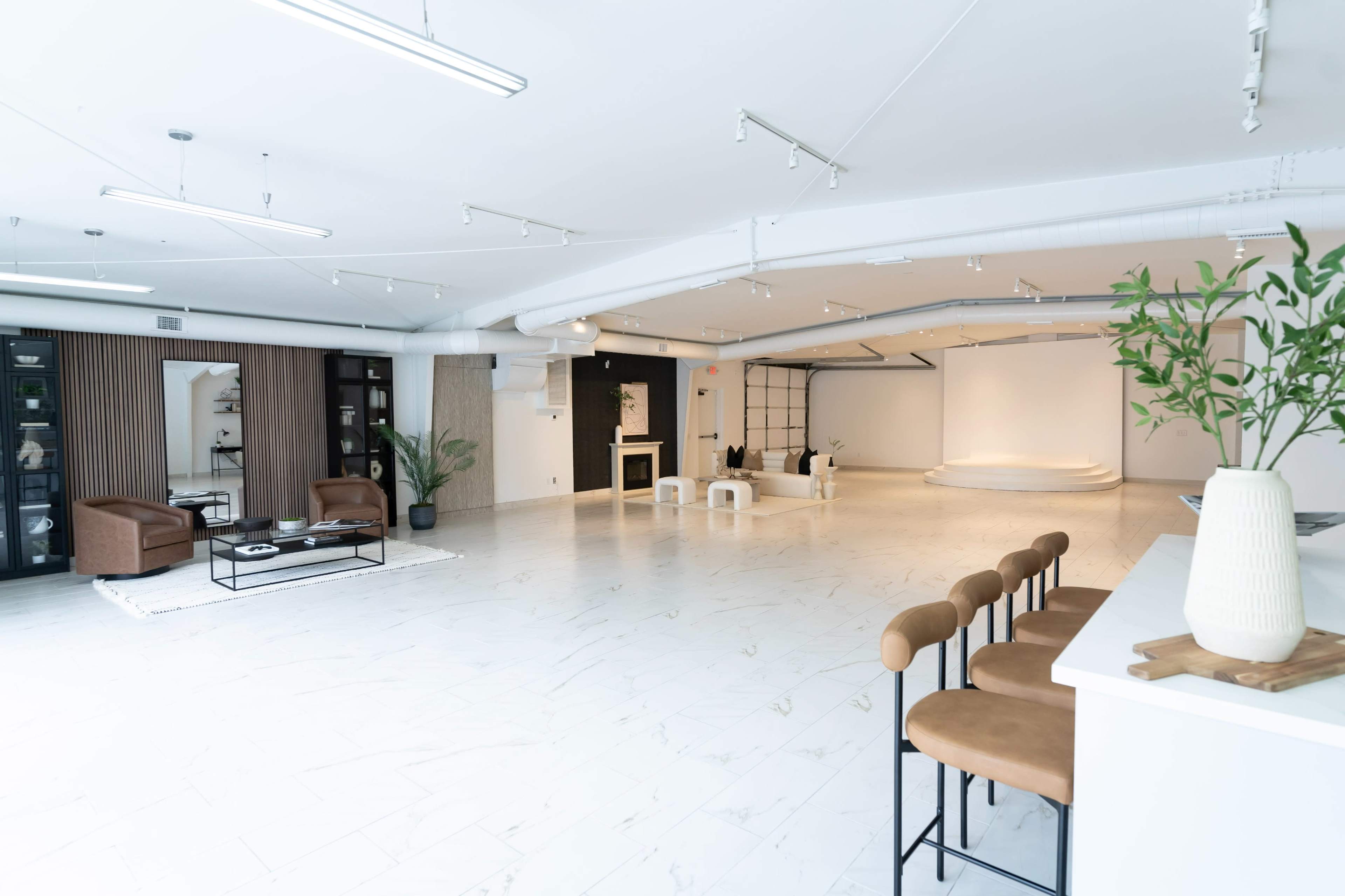 The image shows a spacious, modern studio with light-colored flooring, a minimalist design, and a blank backdrop at one end.