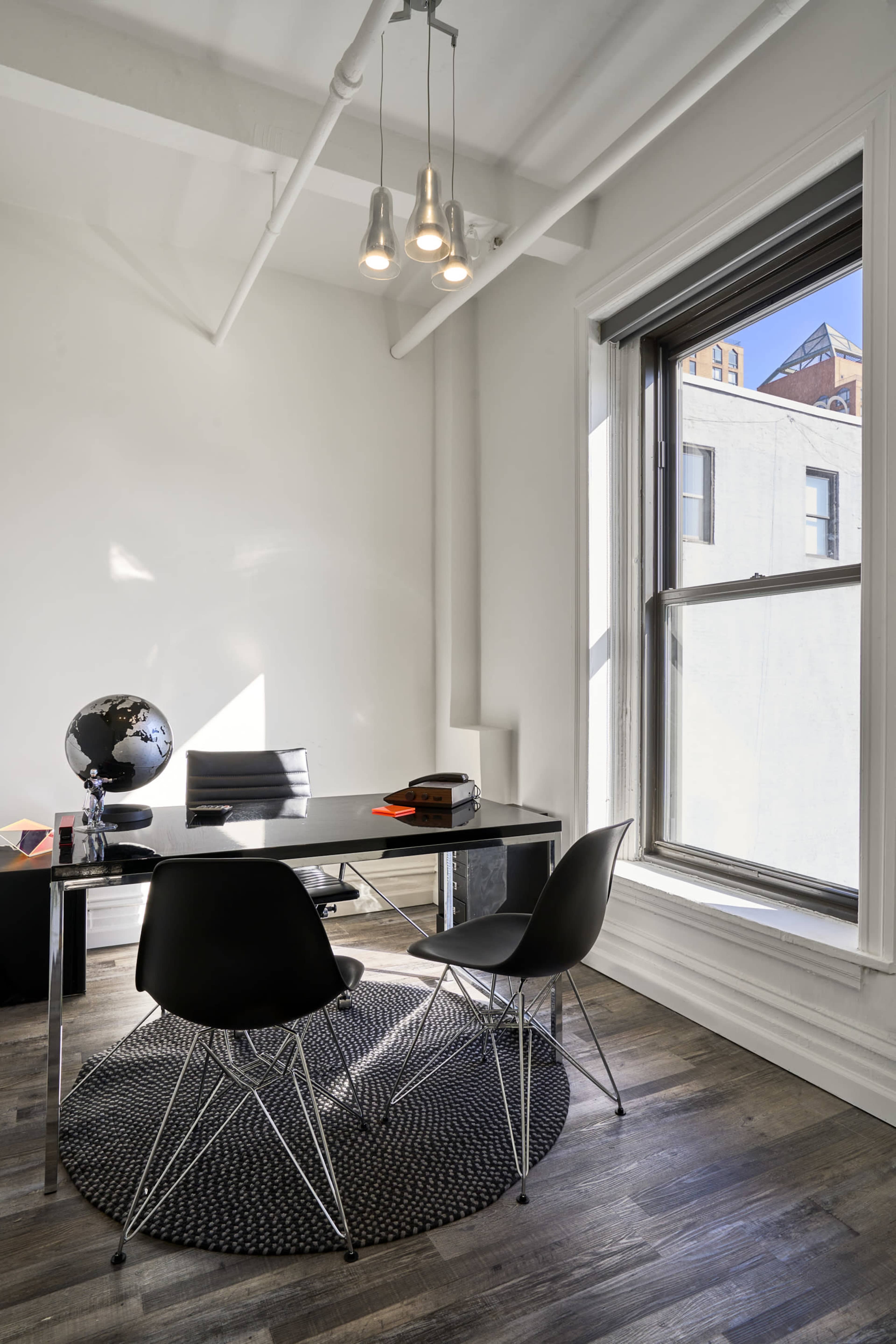 A modern office space featuring a black desk, two black chairs, a globe, and natural light coming through a large window.
