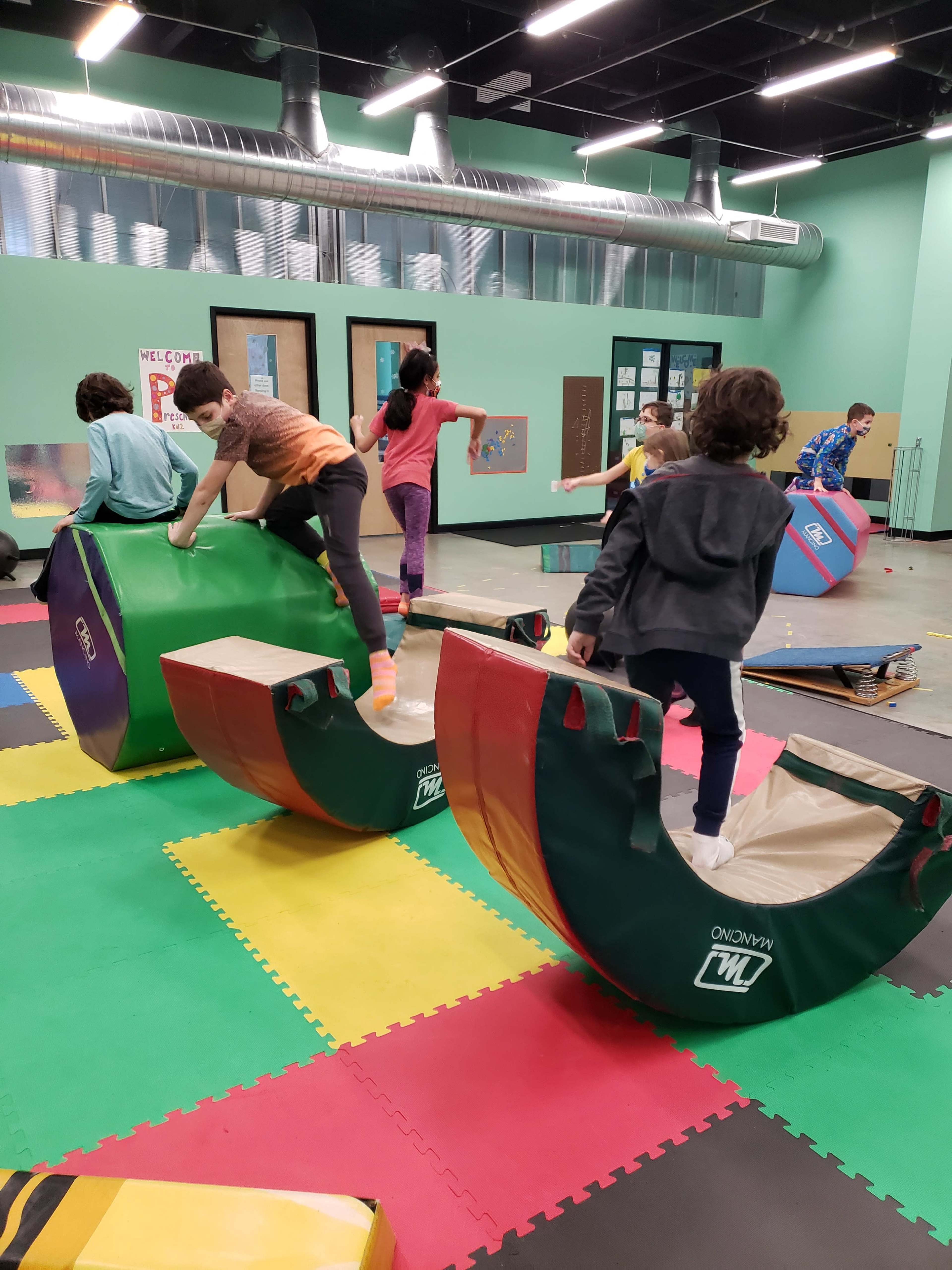 Children are playing on colorful soft climbing structures in an indoor activity area.