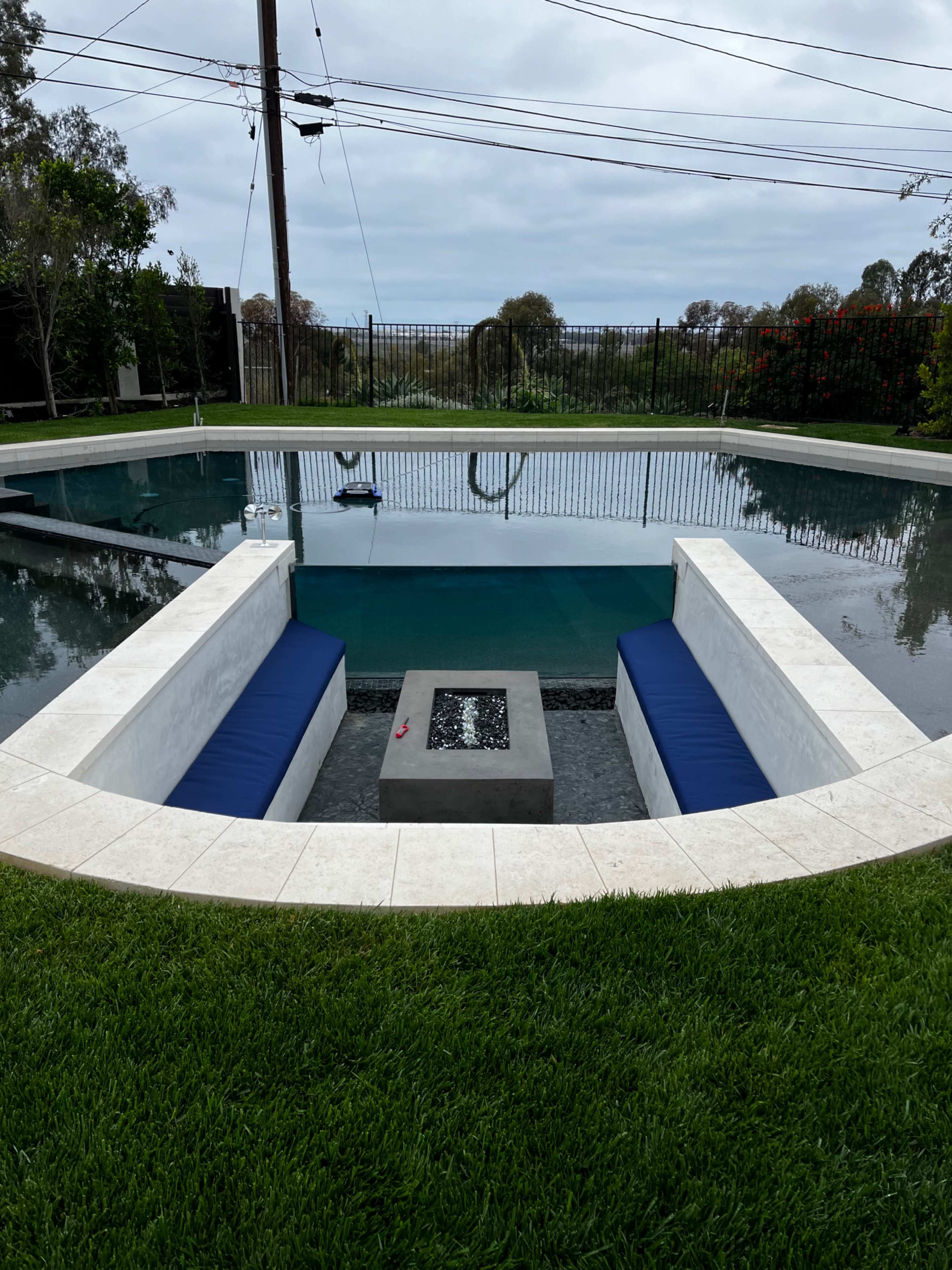 A rectangular swimming pool with a sunken seating area at one end, surrounded by grass and a fencing barrier.