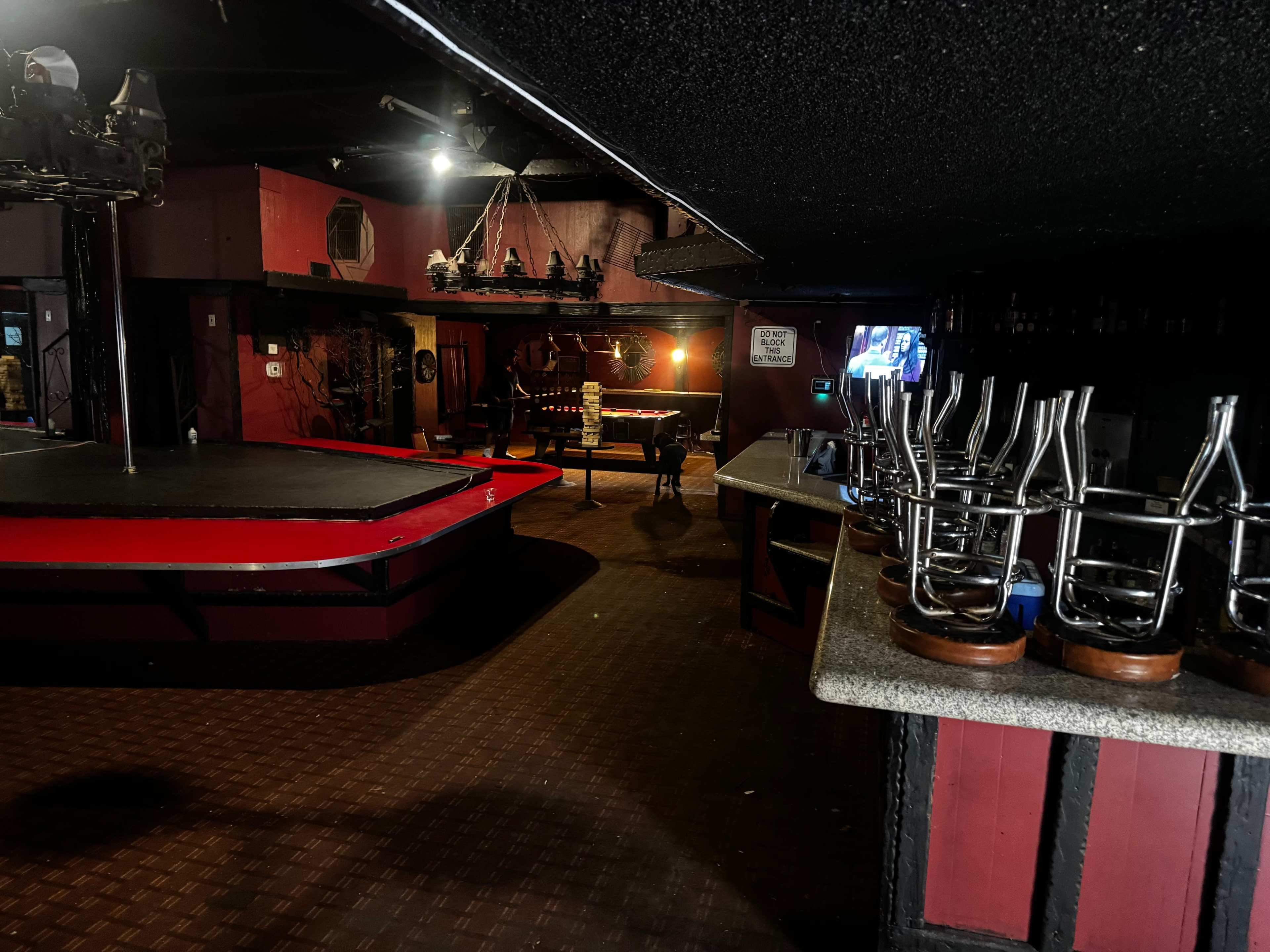 The image shows an empty interior of a nightclub with a stage, bar area, and chairs stacked upside down on tables.
