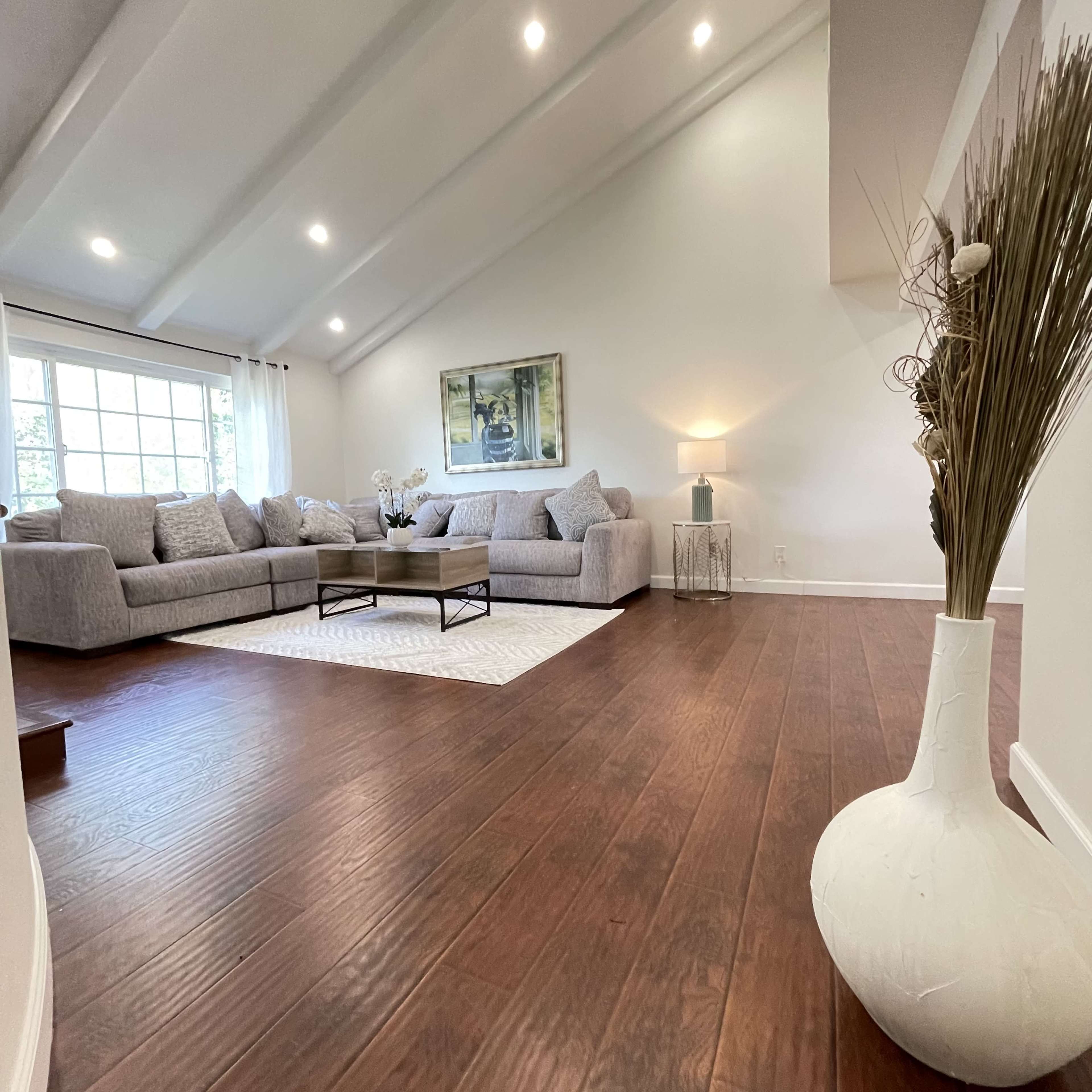 A spacious living room features a large sectional sofa, a coffee table, and a decorative vase by the entrance.