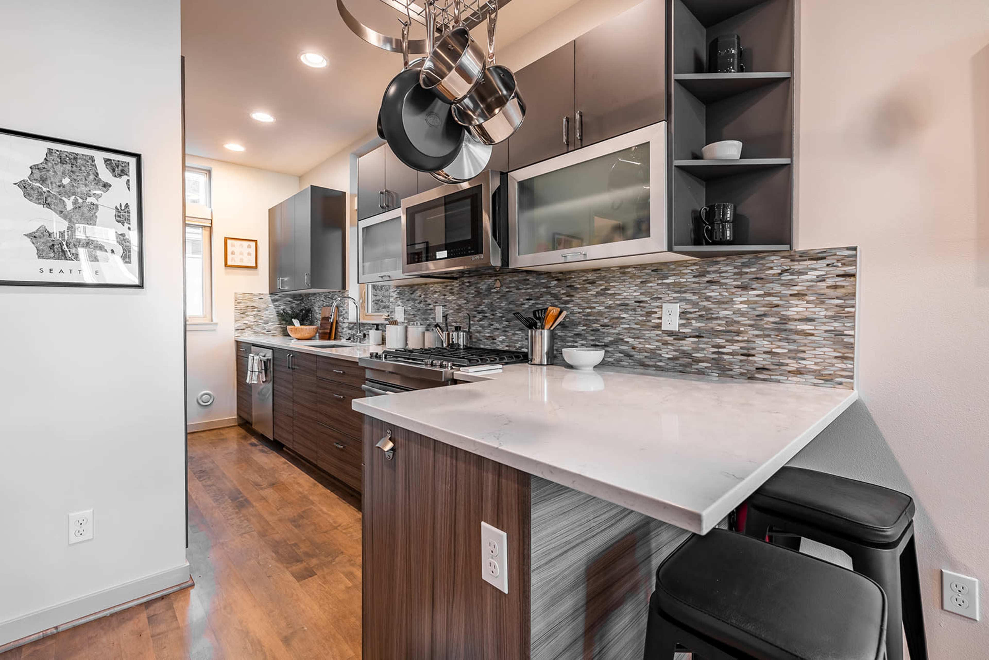 The image shows a modern kitchen featuring dark wood cabinets, stainless steel appliances, and a marble countertop with bar seating.