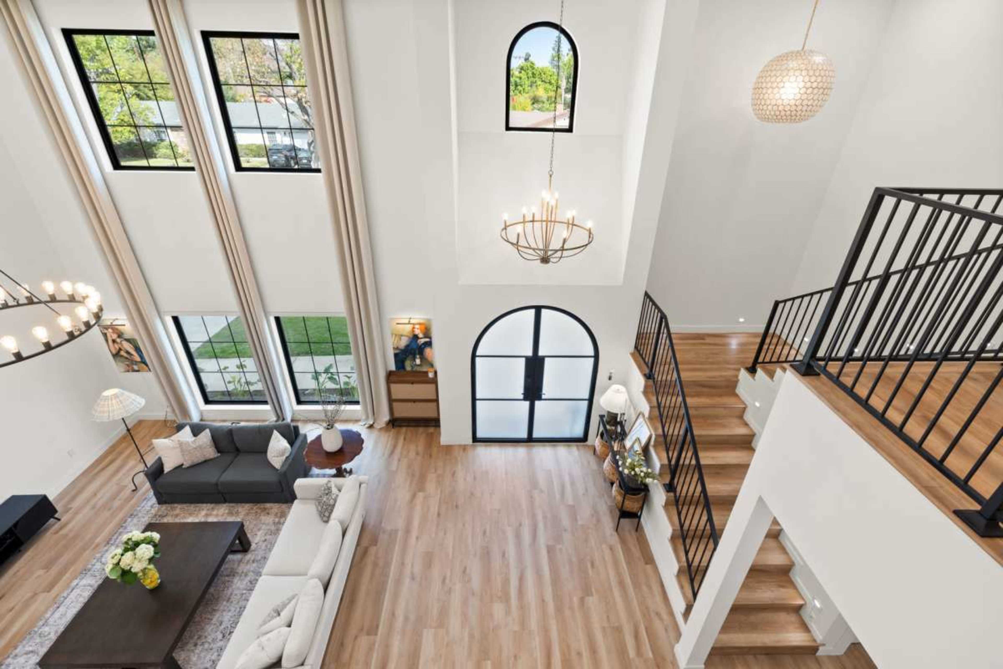 The spacious living room features high ceilings, large windows, and a staircase leading to an upper level.