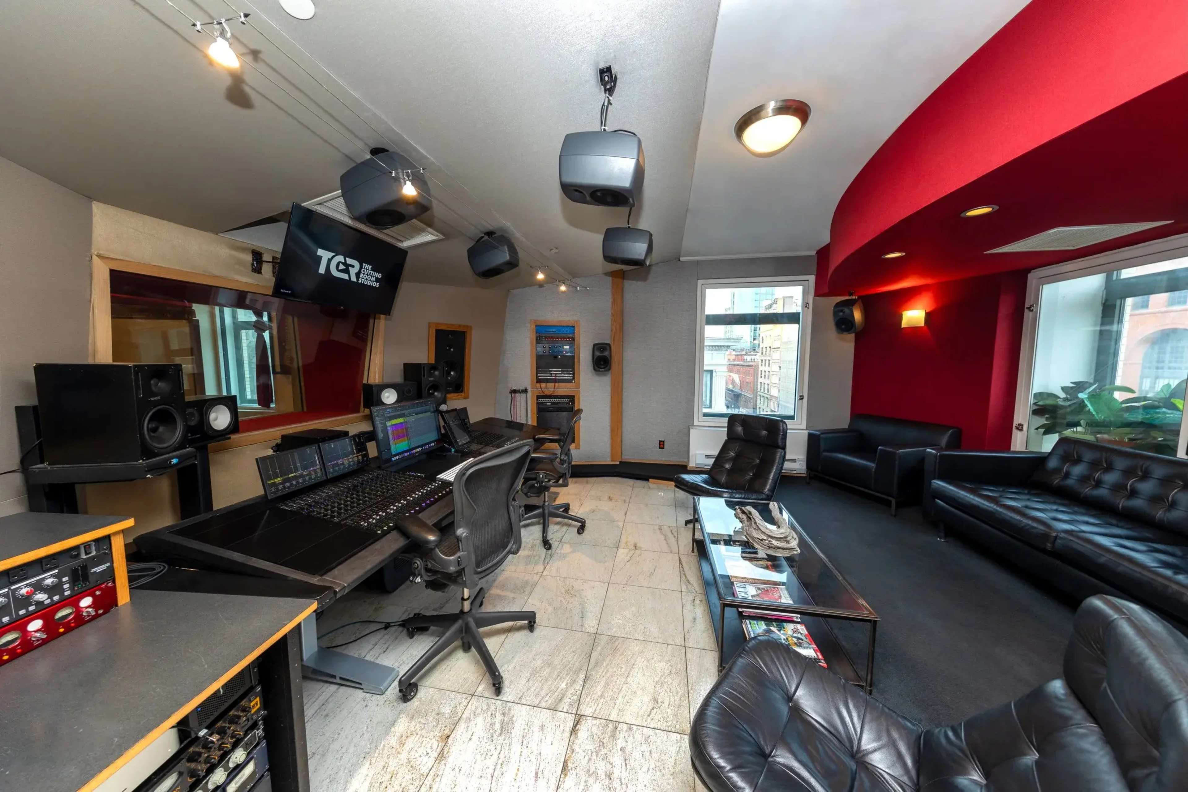 The image shows a modern recording studio featuring a mixing console, multiple speakers, and seating areas.