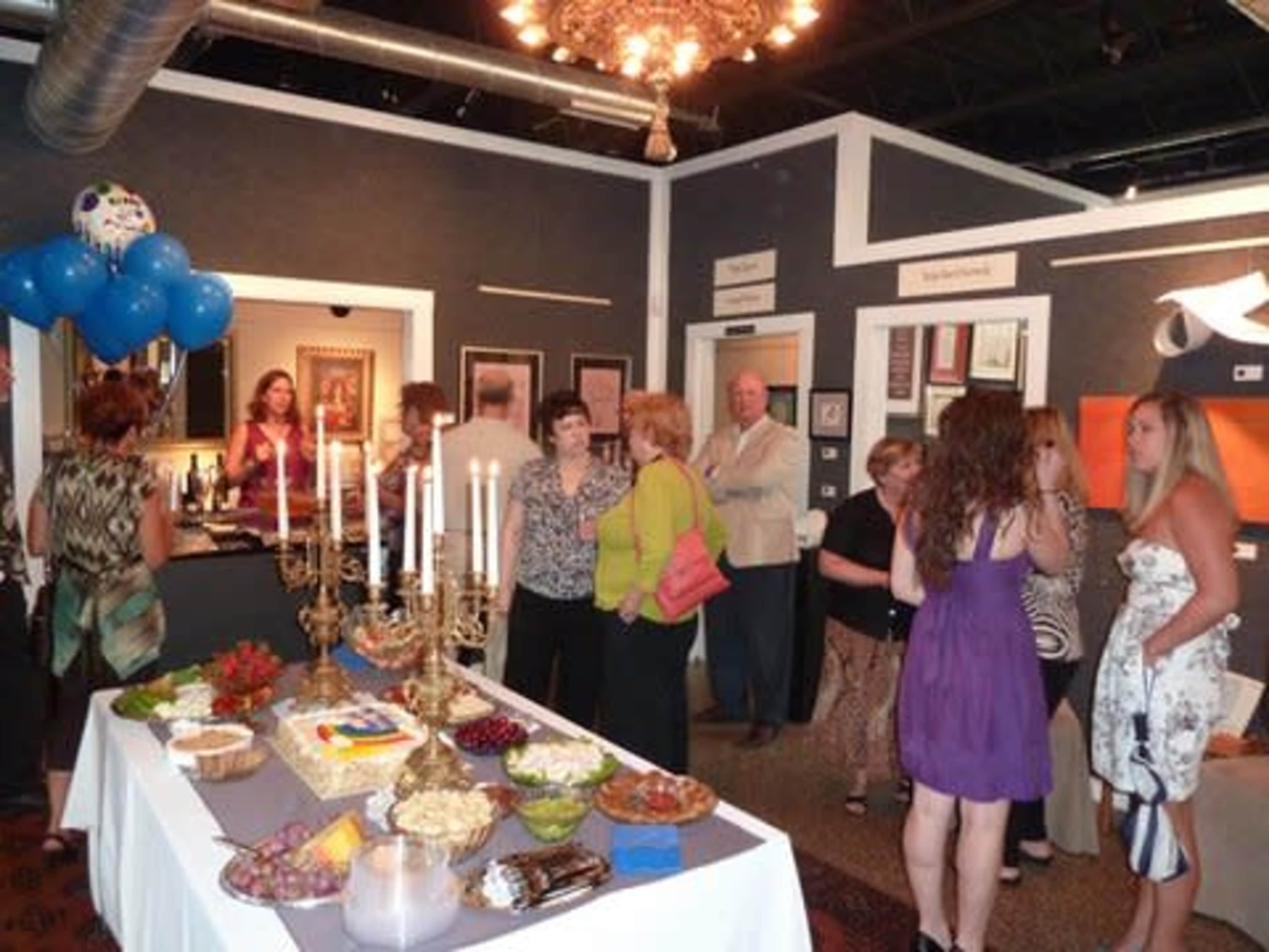 A group of people socialize at an art gallery opening, surrounded by food and decorations.