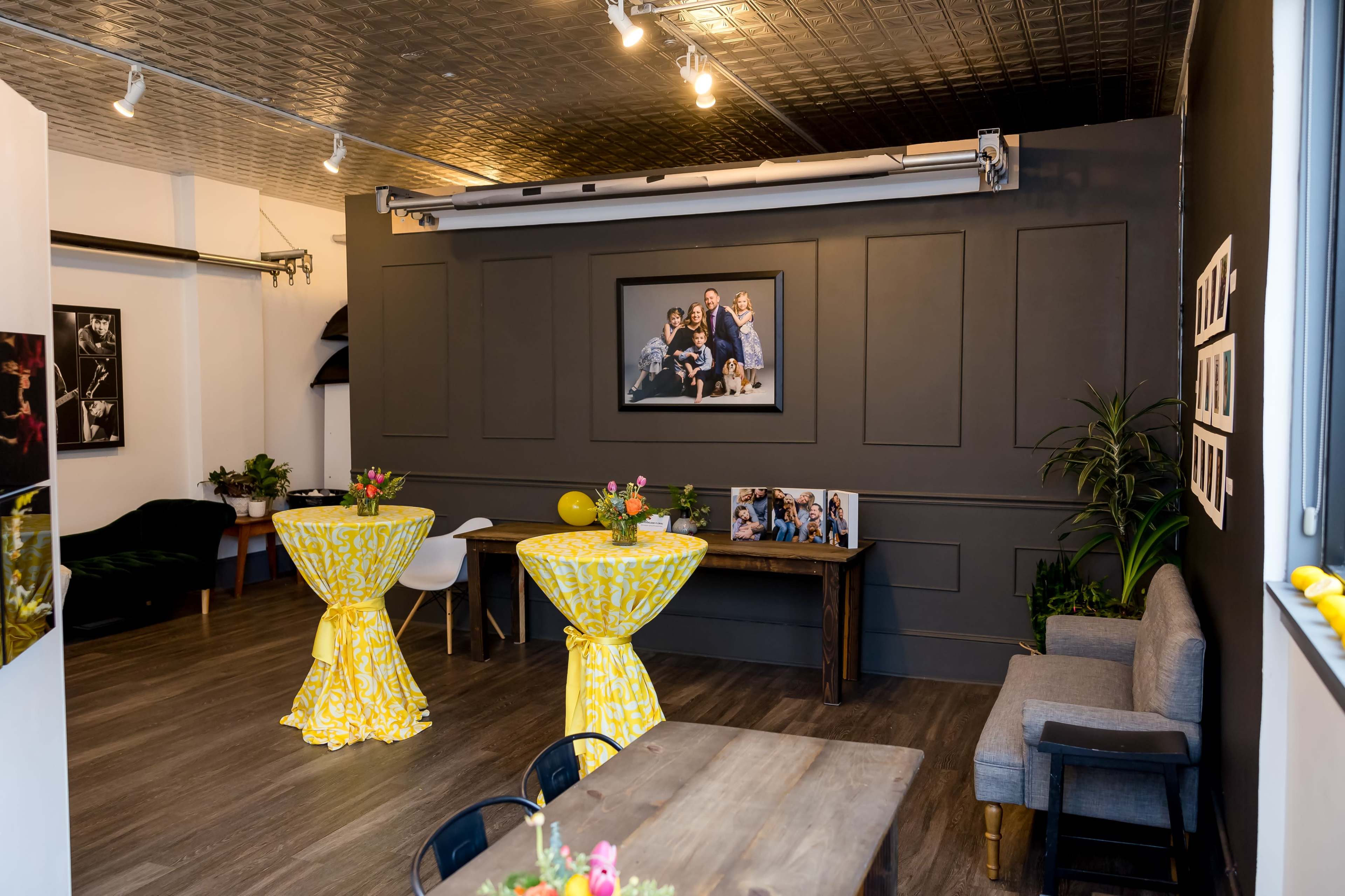 A modern interior space with two tables draped in yellow tablecloths, a gray sofa, and framed photographs on the walls.