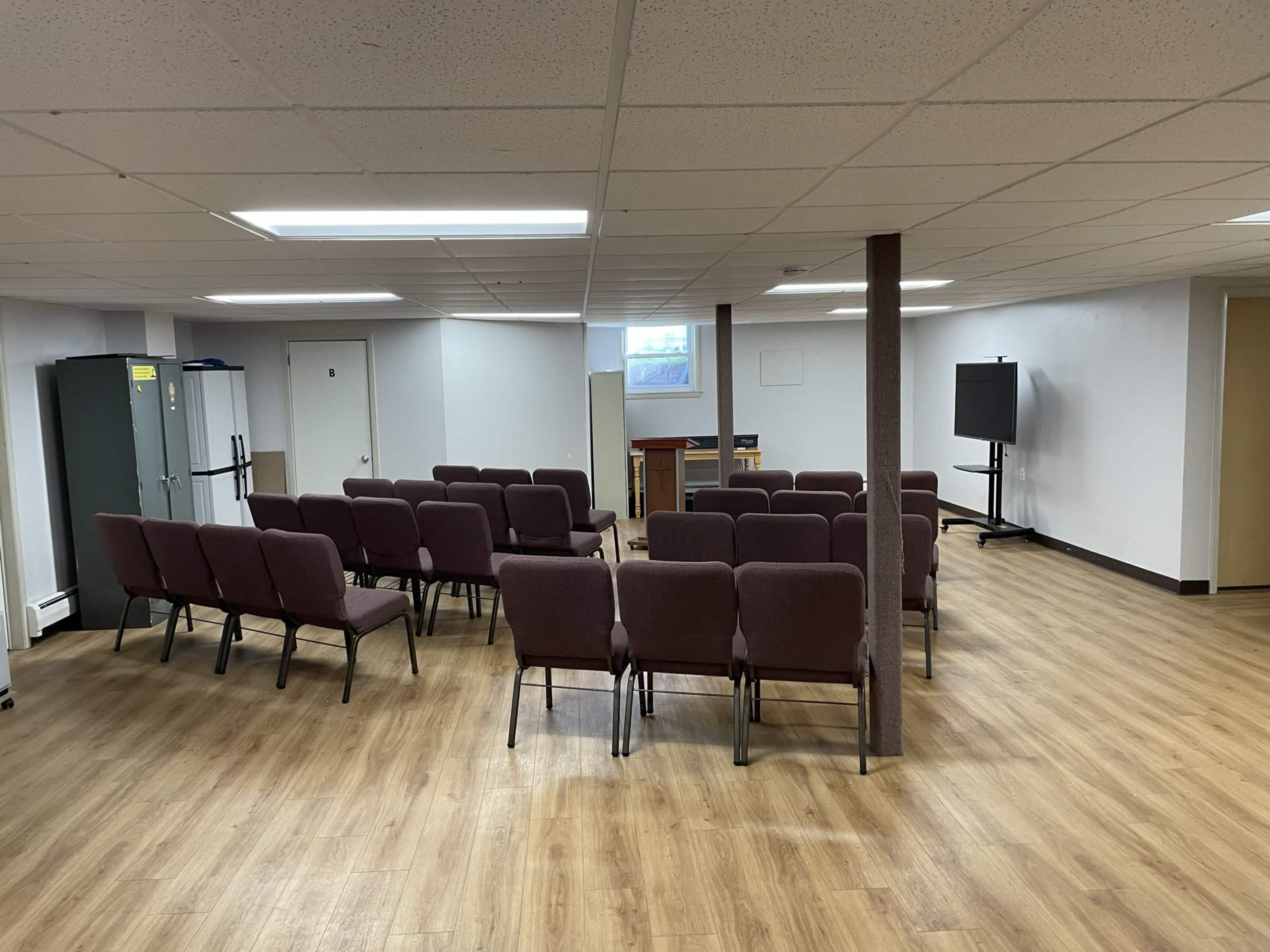 A meeting room with several rows of brown chairs facing a projector screen and a wooden podium.