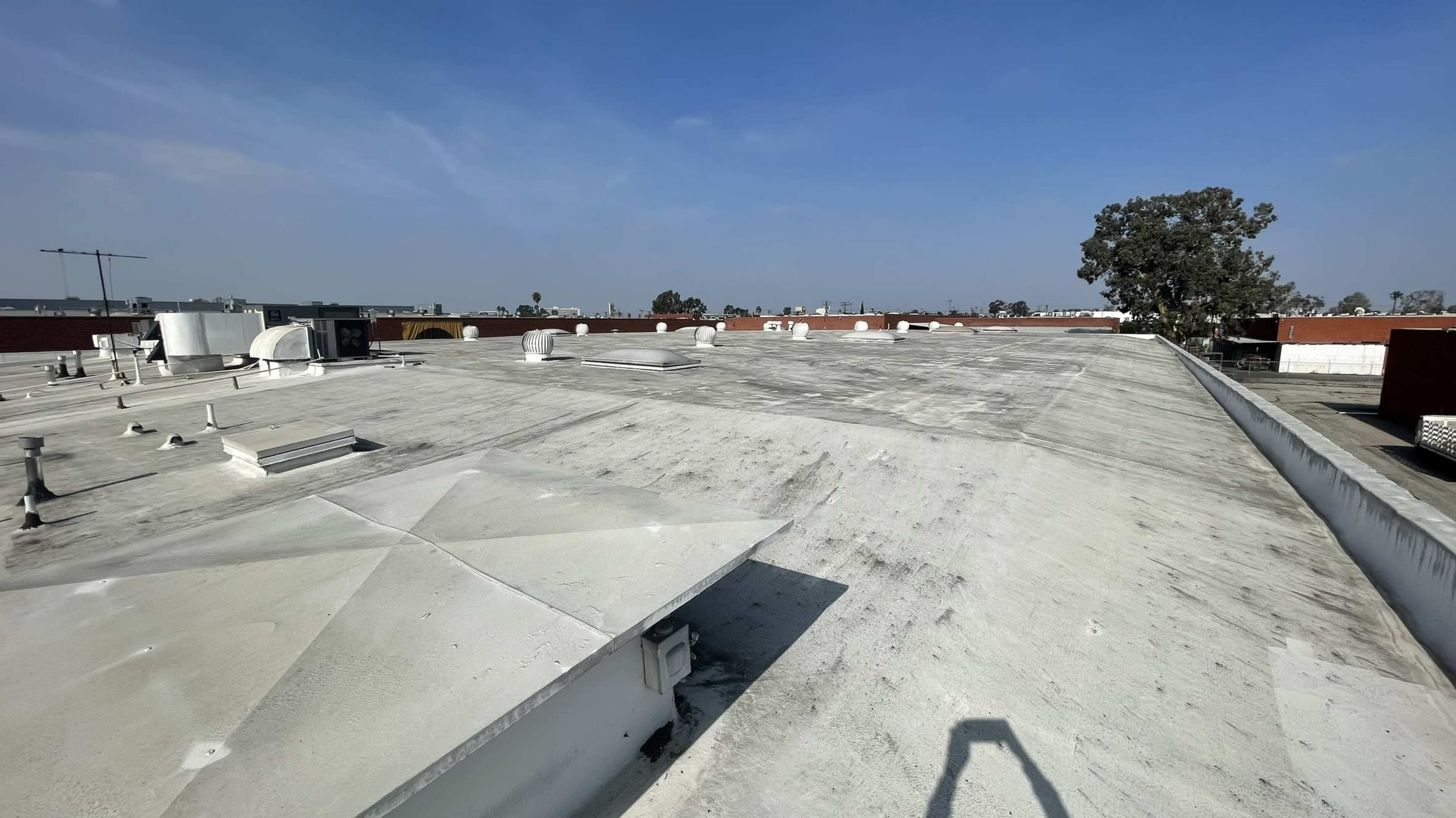 A flat, white rooftop with a few vents and structures, under a clear blue sky.