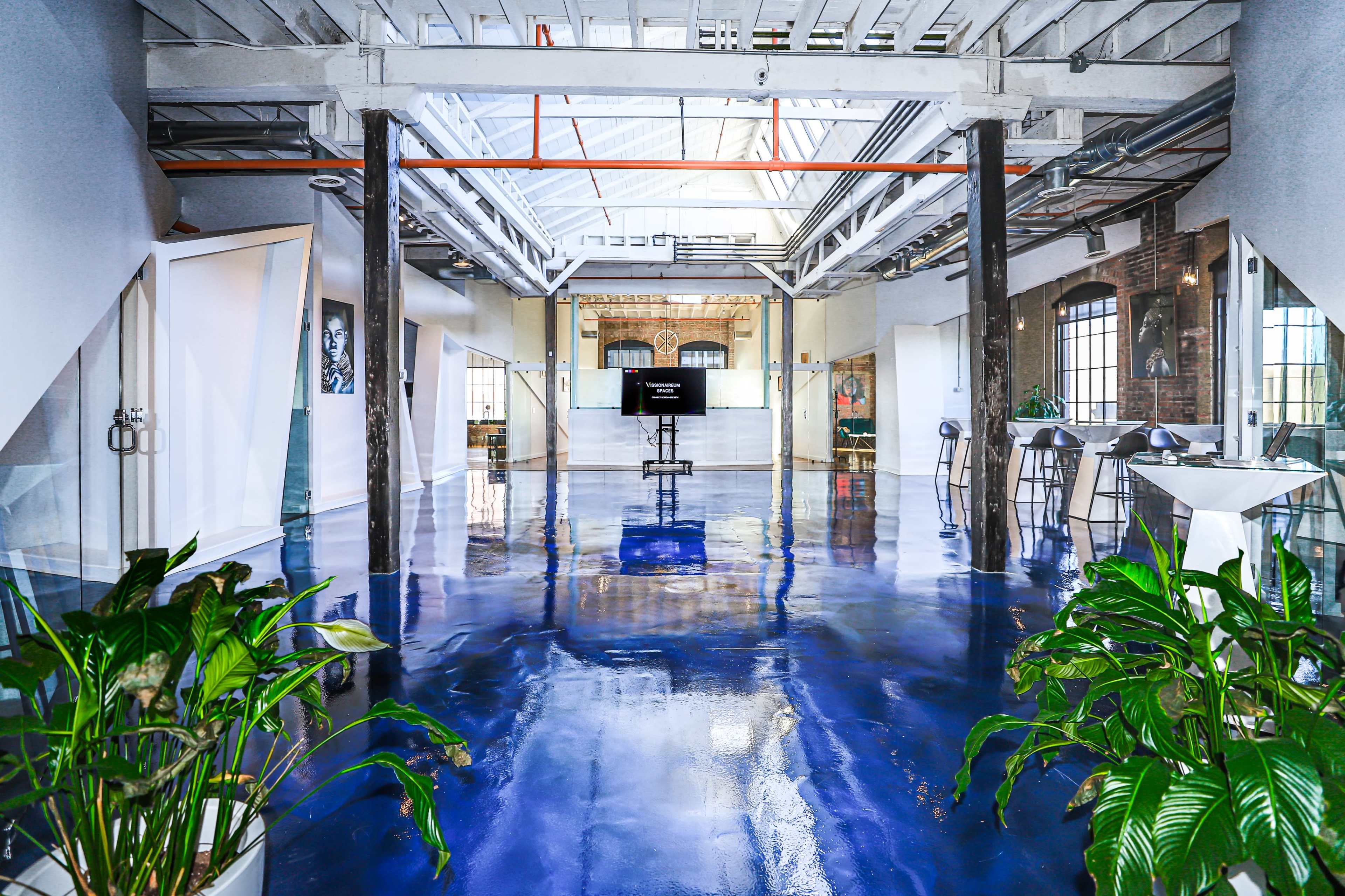 A spacious, modern interior of a building with polished blue floors, large windows, and various plants.