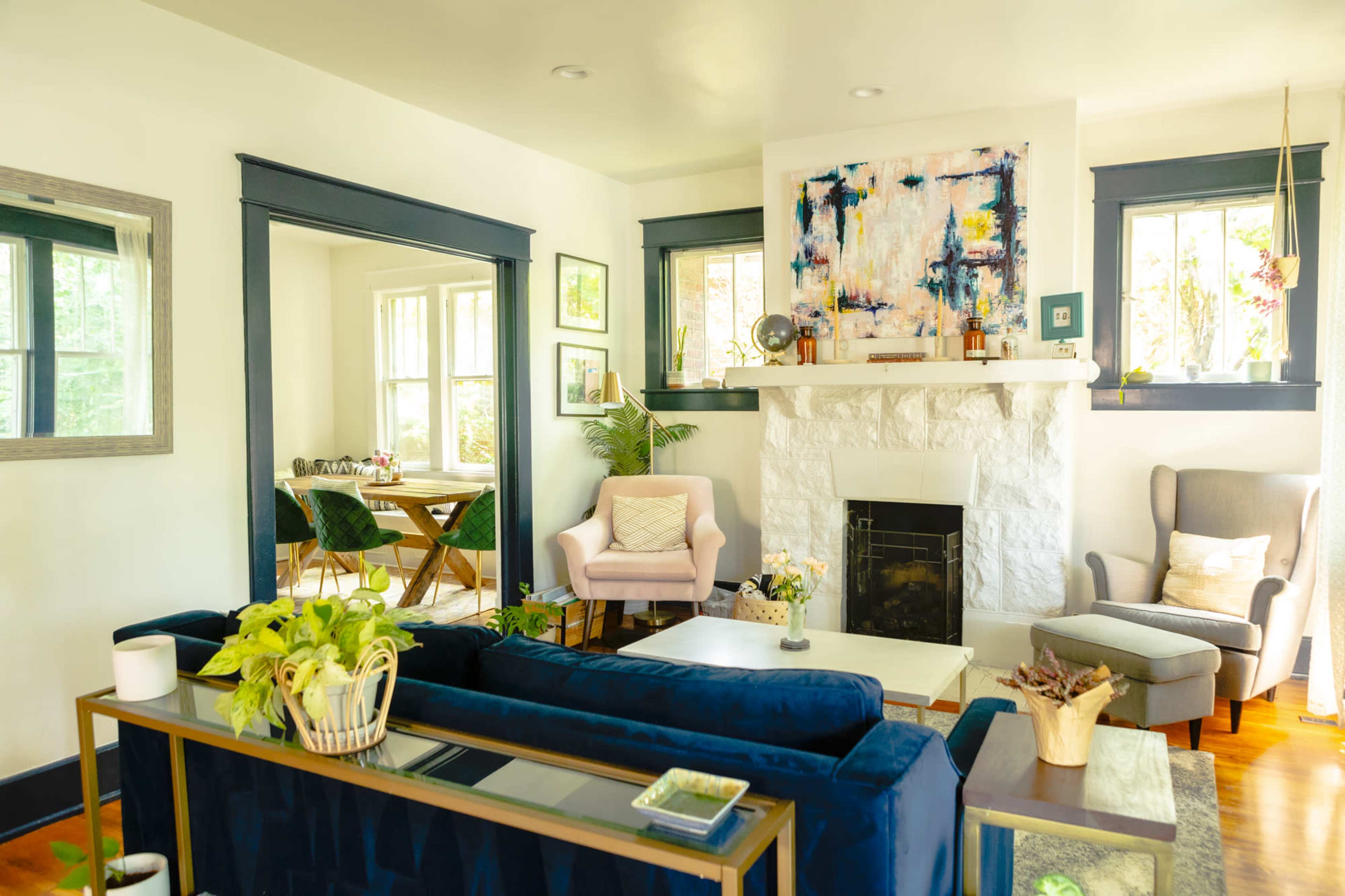 A bright living room with a blue sofa, a stone fireplace, and a dining area visible in the background.