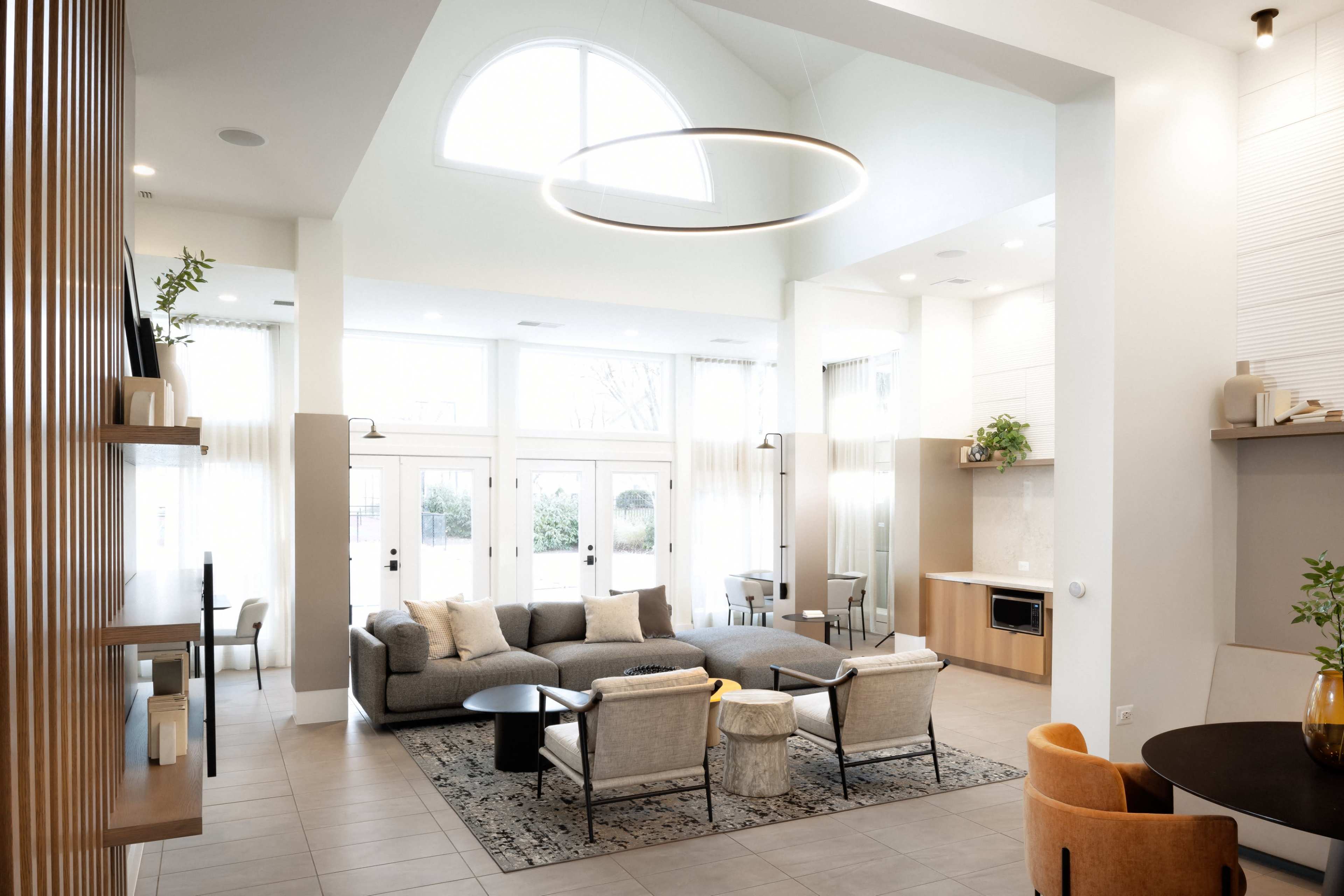 A spacious modern living area features a large sectional sofa, circular light fixture, and multiple seating arrangements near large windows.