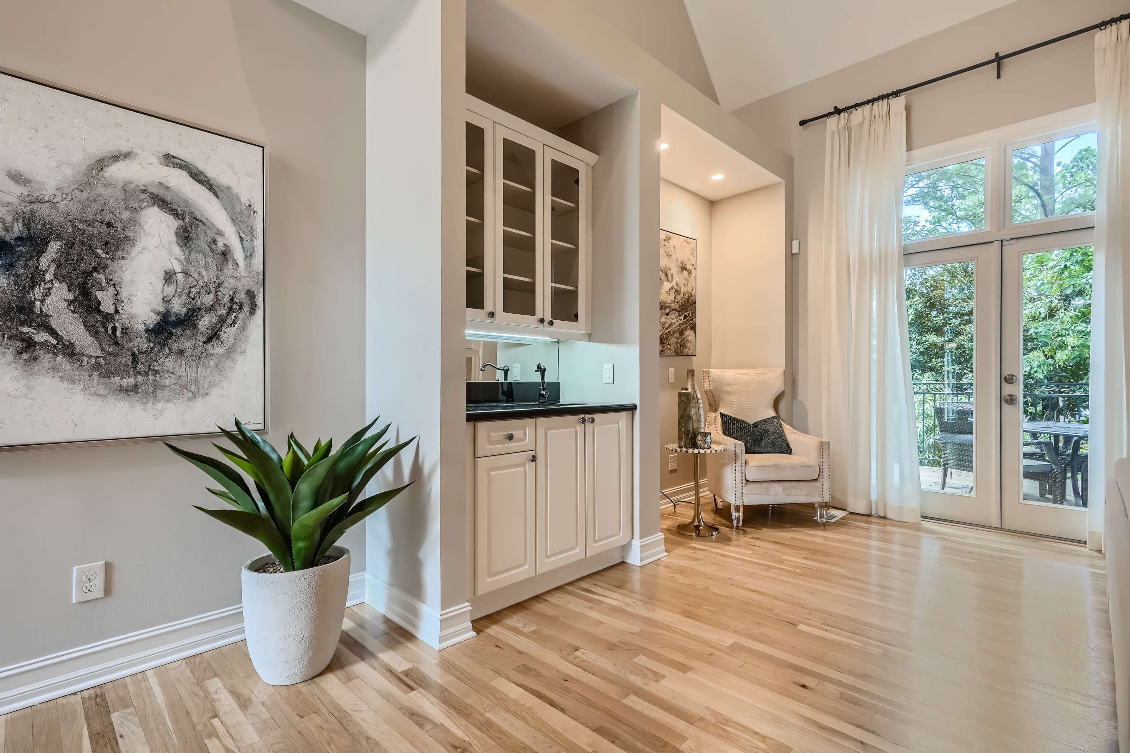 A modern interior features a wet bar with cabinetry, a cozy armchair, and large windows opening to an outdoor space.