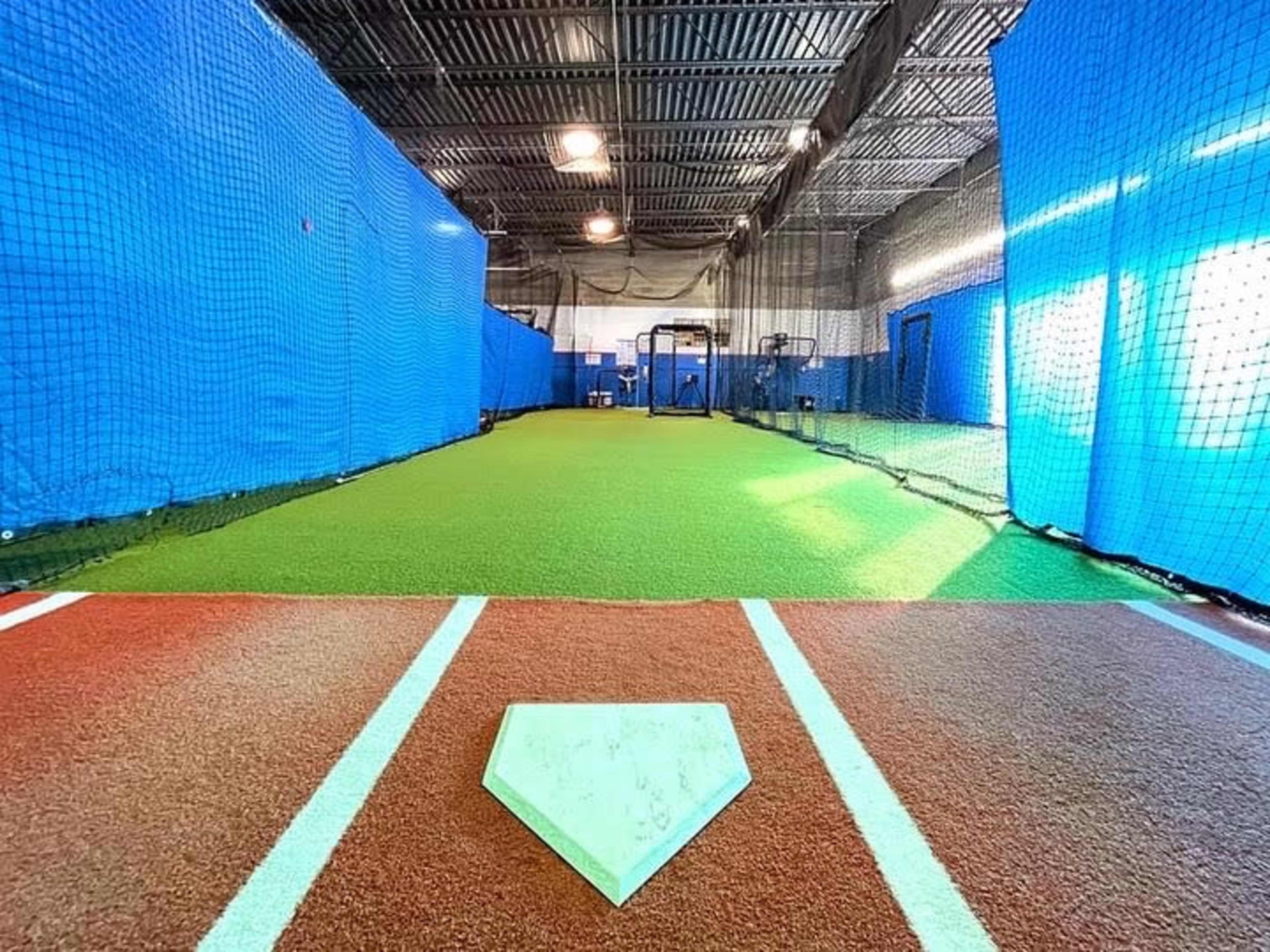 An indoor baseball batting cage with green turf and blue netting along the sides.