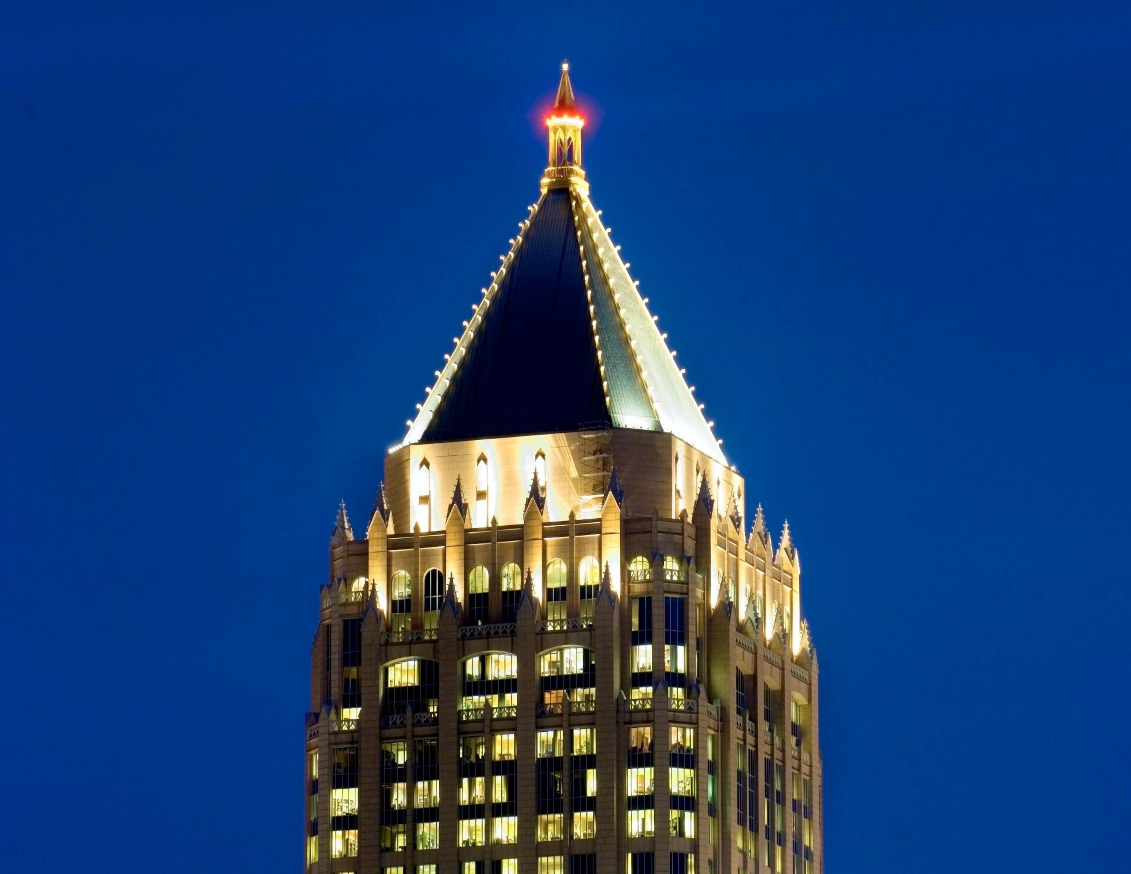 The illuminated peak of a tall skyscraper against a dark blue night sky.
