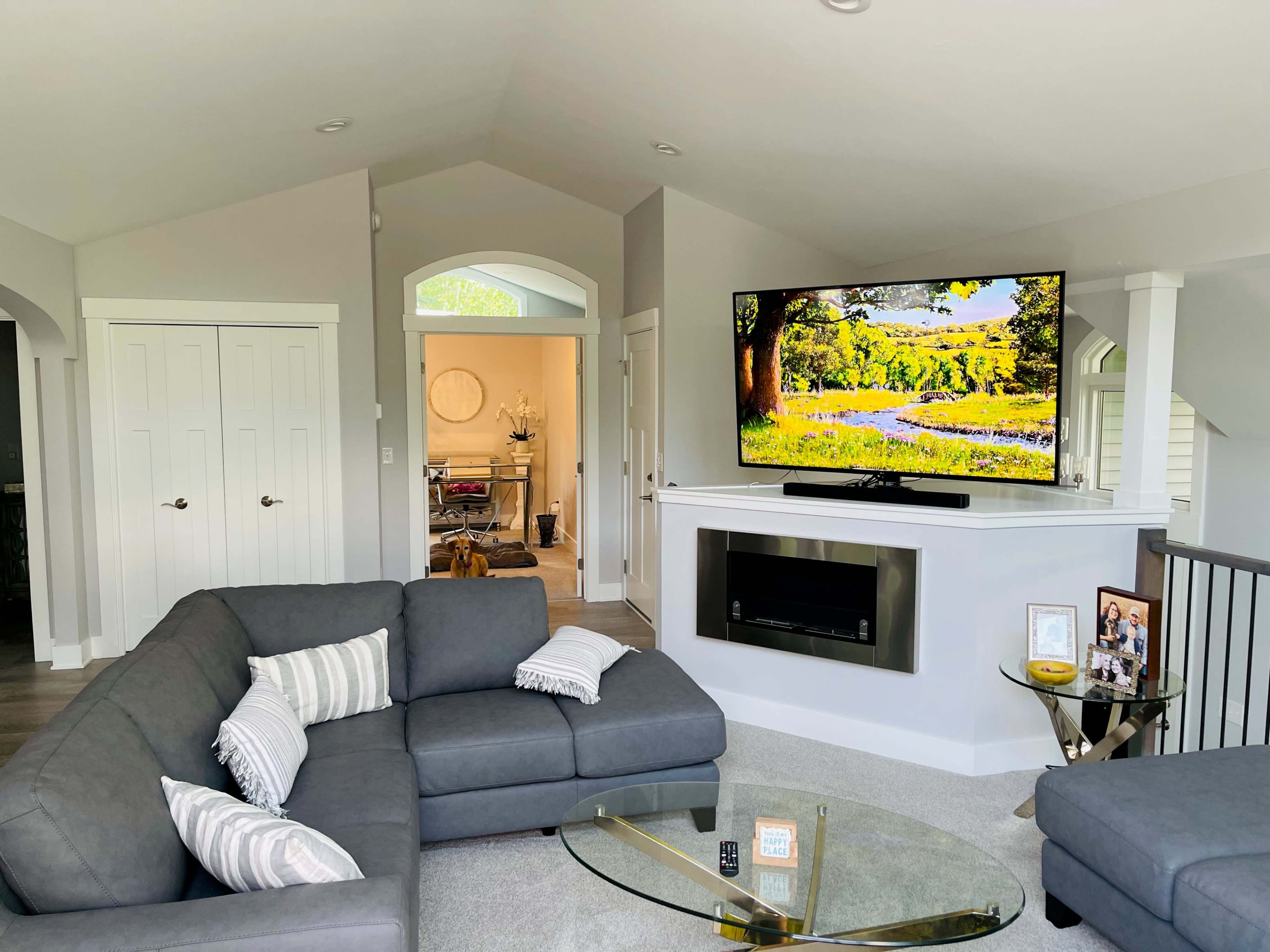 A modern living room featuring a gray sectional sofa, a mounted flat-screen television, and a glass coffee table.
