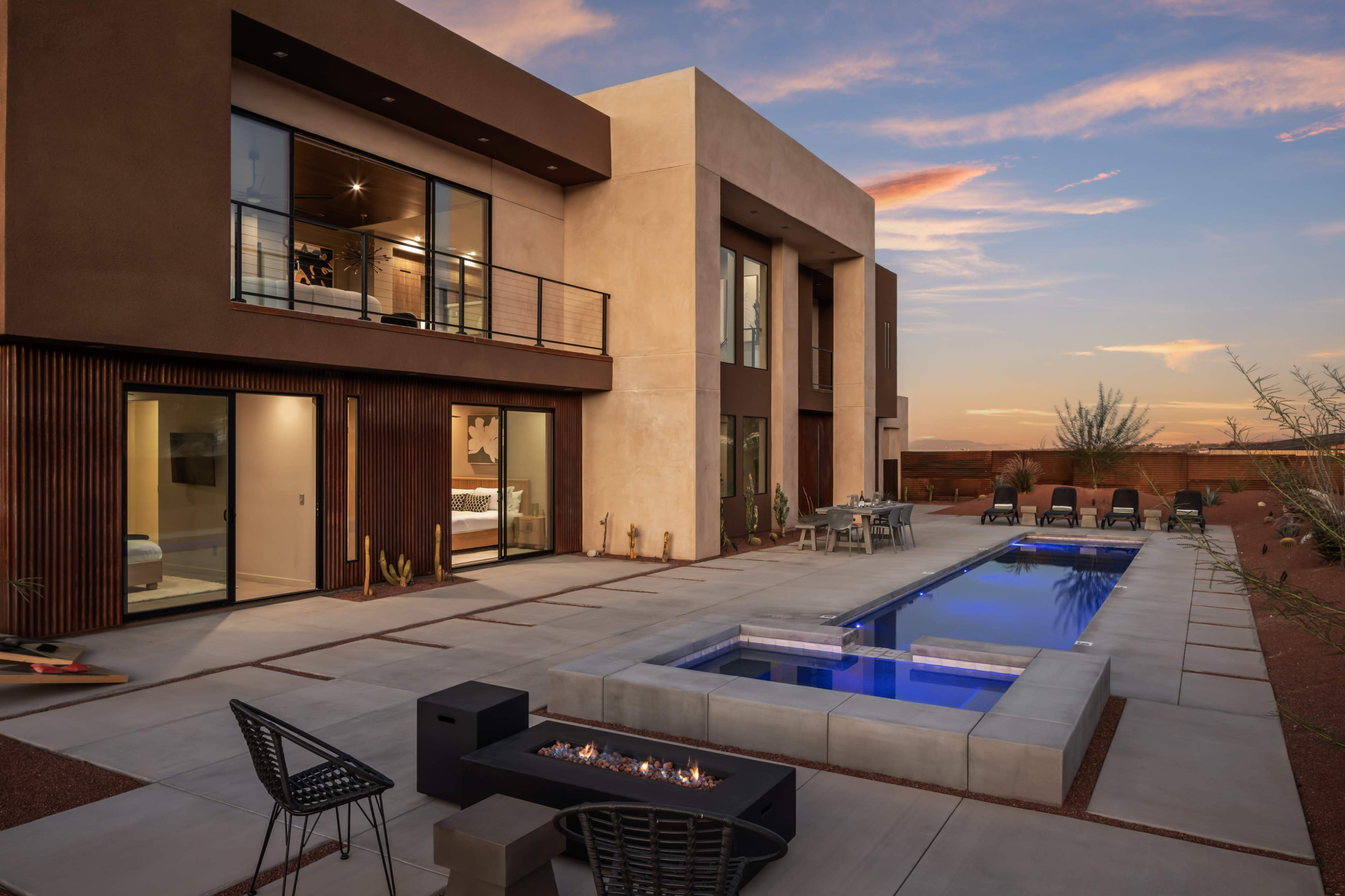 The image shows a modern two-story house with large glass windows, featuring a rectangular swimming pool and a fire pit in the outdoor area.
