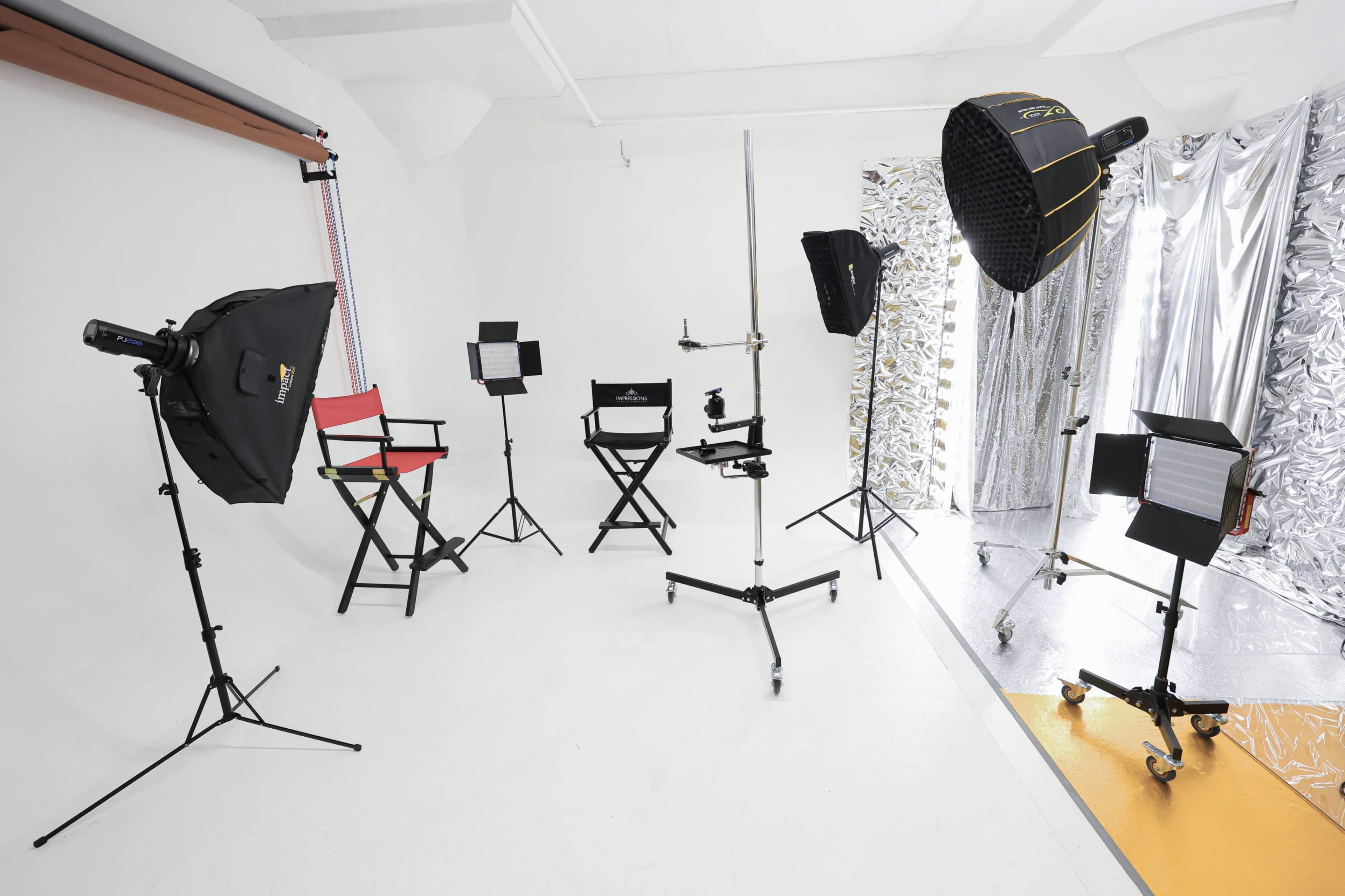 A professional photography studio setup with various lighting equipment, tripods, and camera gear arranged around a clean, white background.
