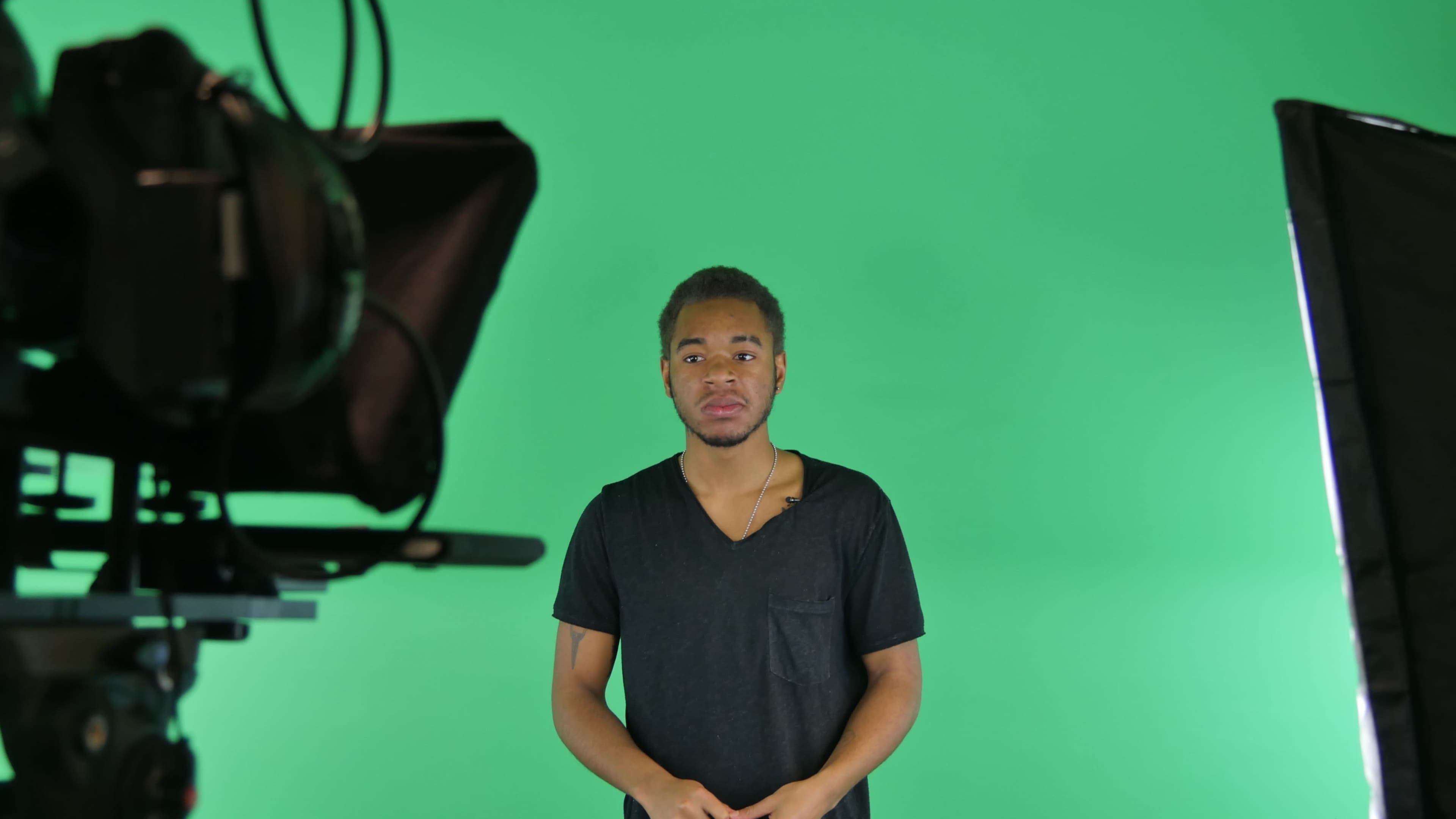 A person stands in front of a green screen while a camera captures the scene.