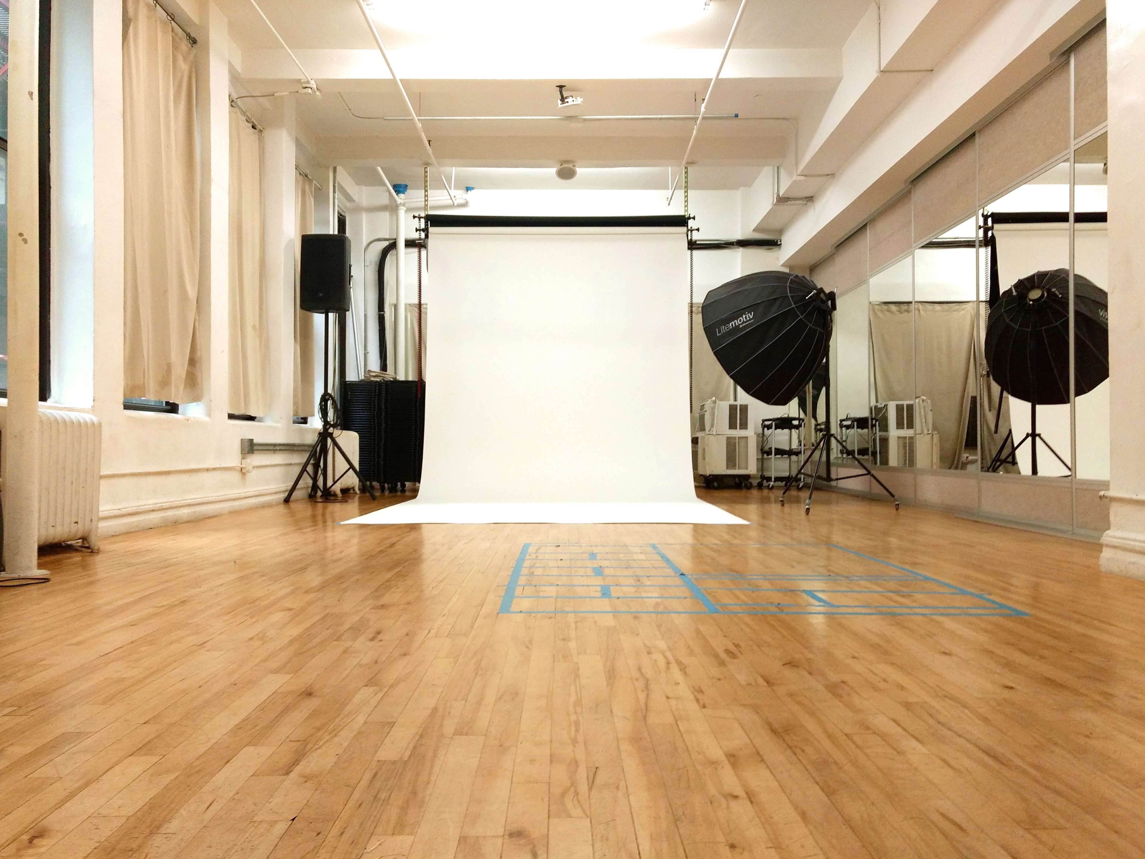 A photography studio with a white backdrop, large softbox lights on either side, and polished wooden flooring.