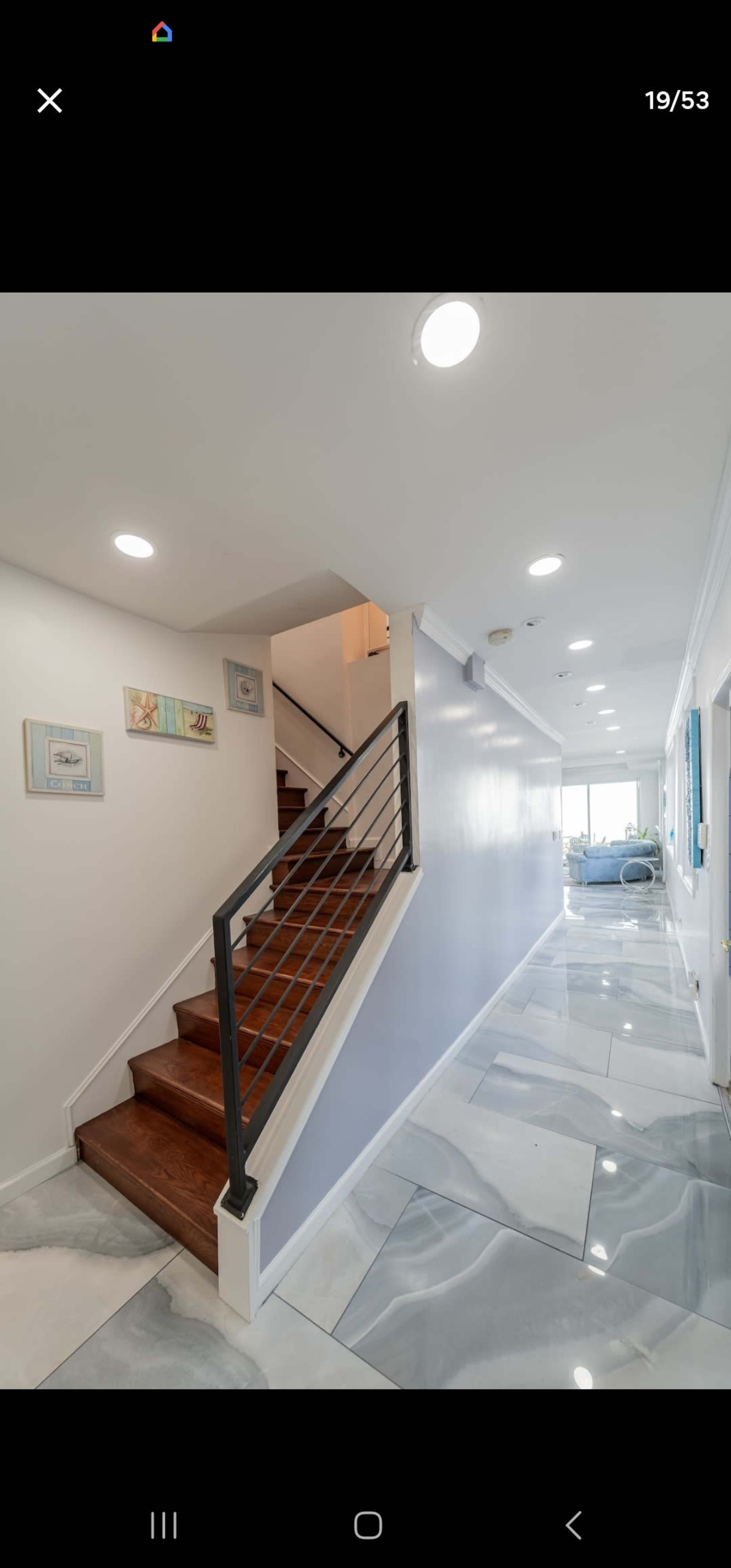 The image shows a modern hallway with a staircase on the left, featuring light-colored walls and polished marble flooring.